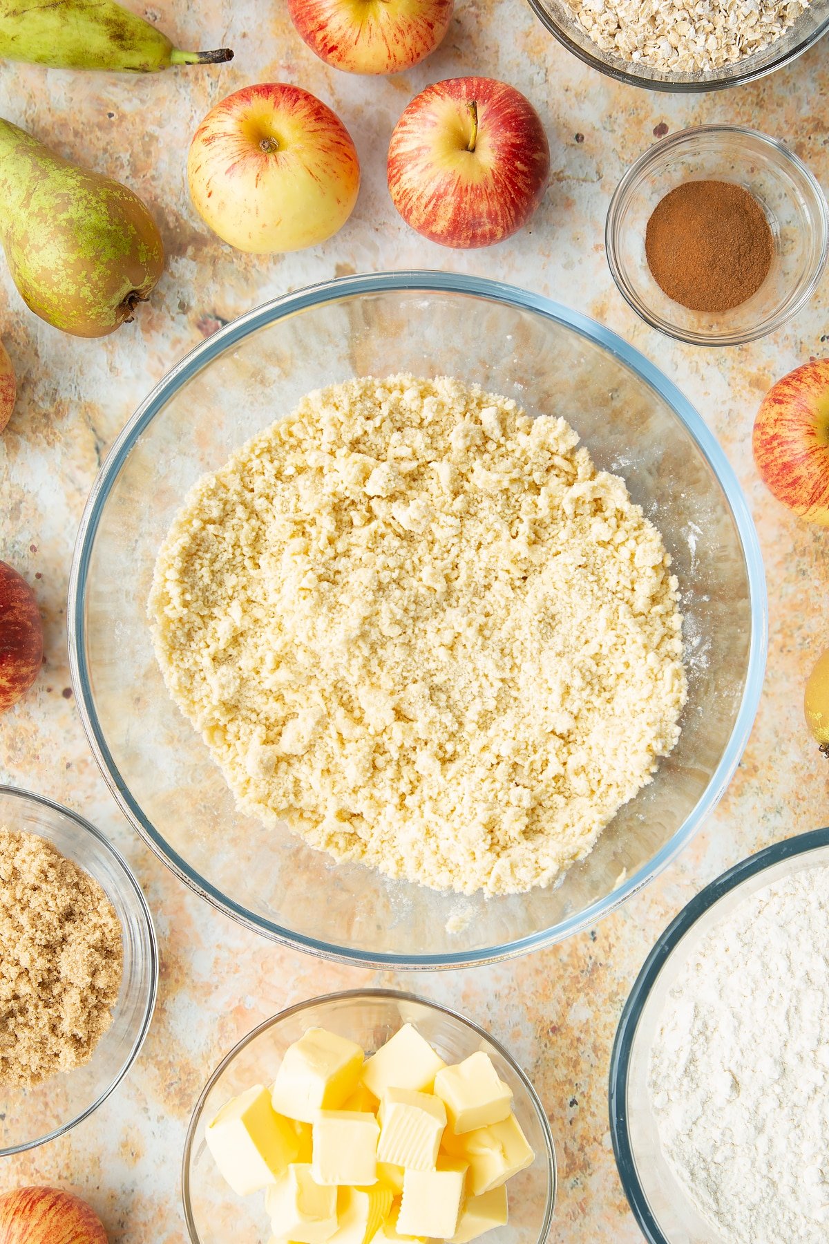 Flour and butter rubbed together in a mixing bowl. Ingredients to make easy apple pear crumble surround the bowl.