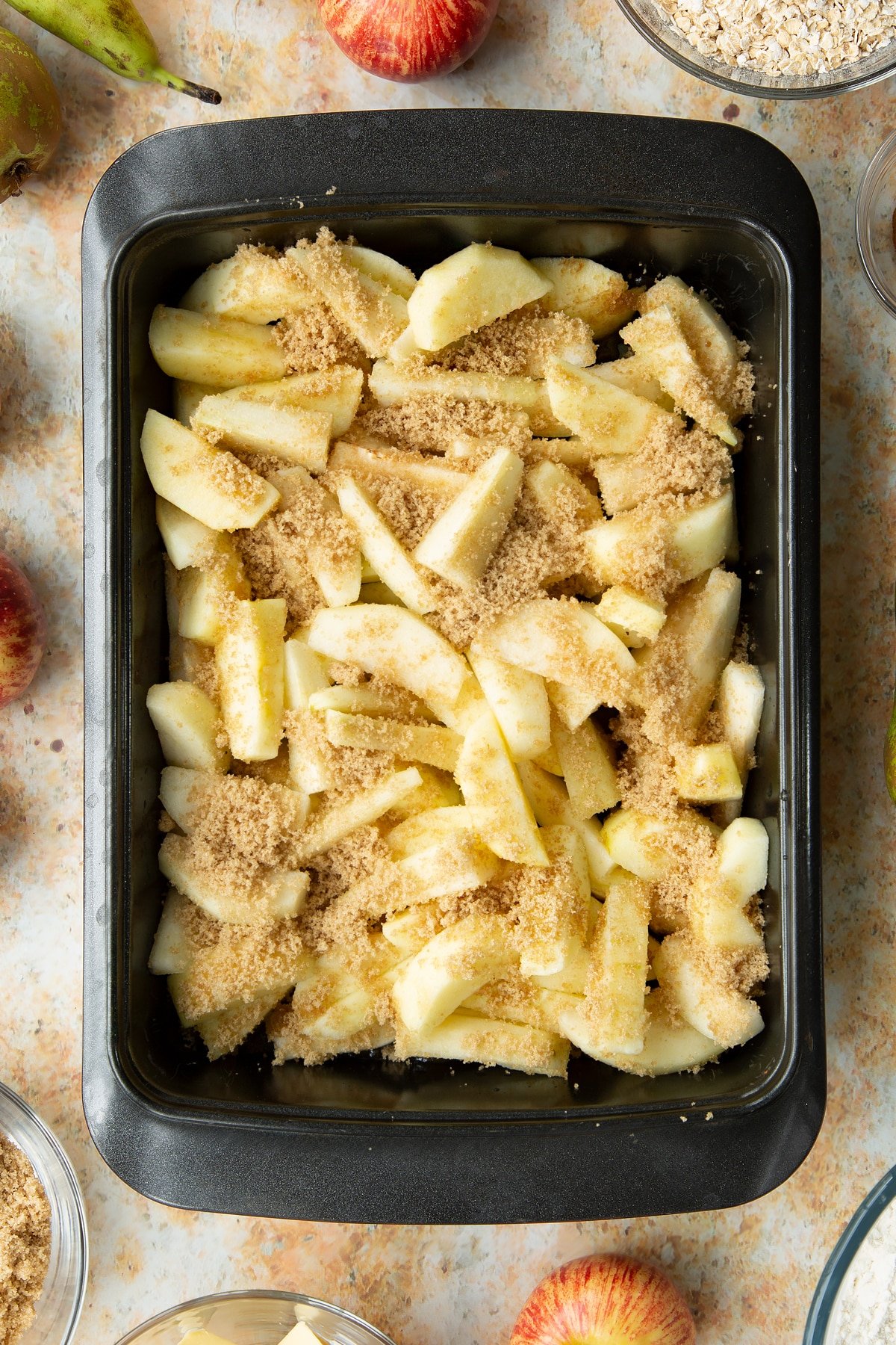 Peeled apple and pear wedges, topped with light brown sugar in a greased tray.