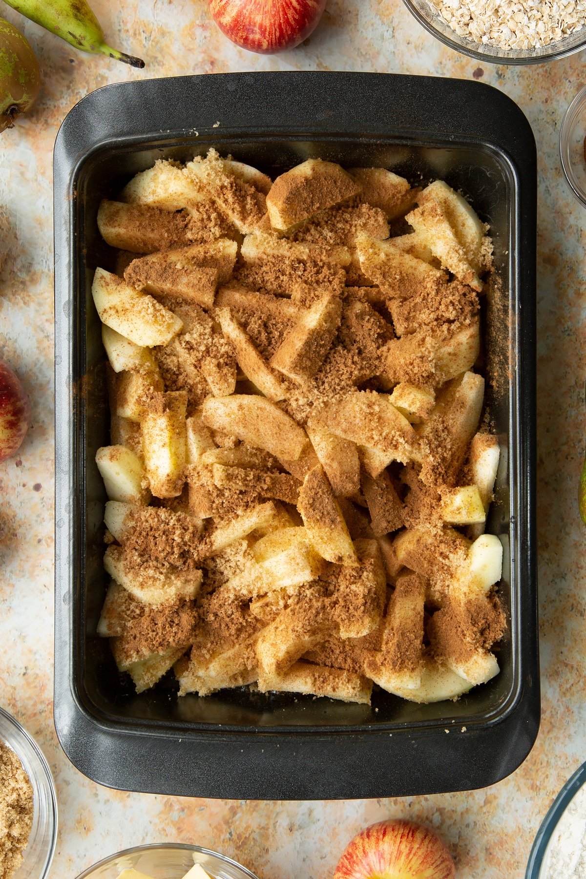 Peeled apple and pear wedges, topped with light brown sugar and cinnamon in a greased tray.