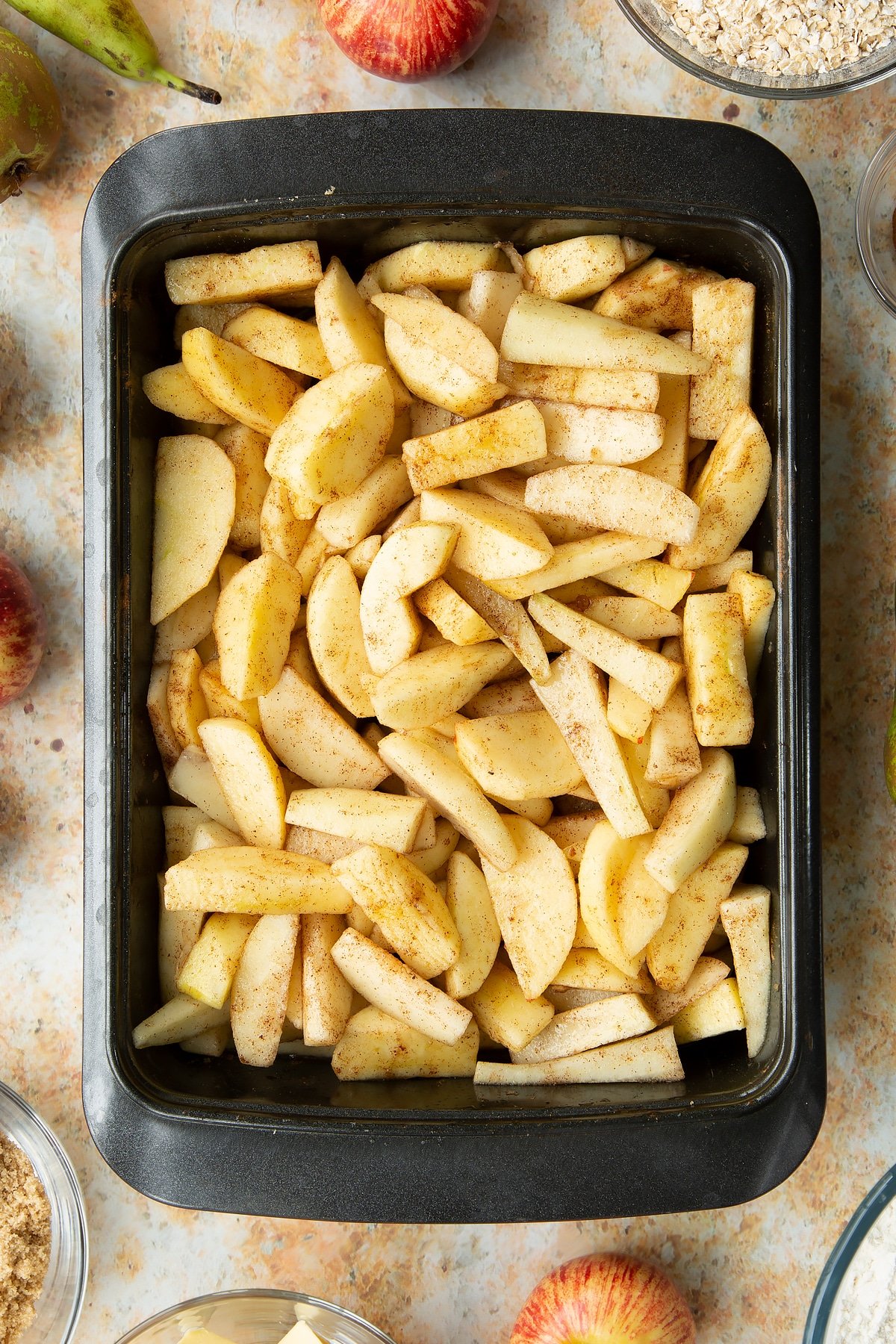 Peeled apple and pear wedges mixed with light brown sugar and cinnamon in a greased tray.