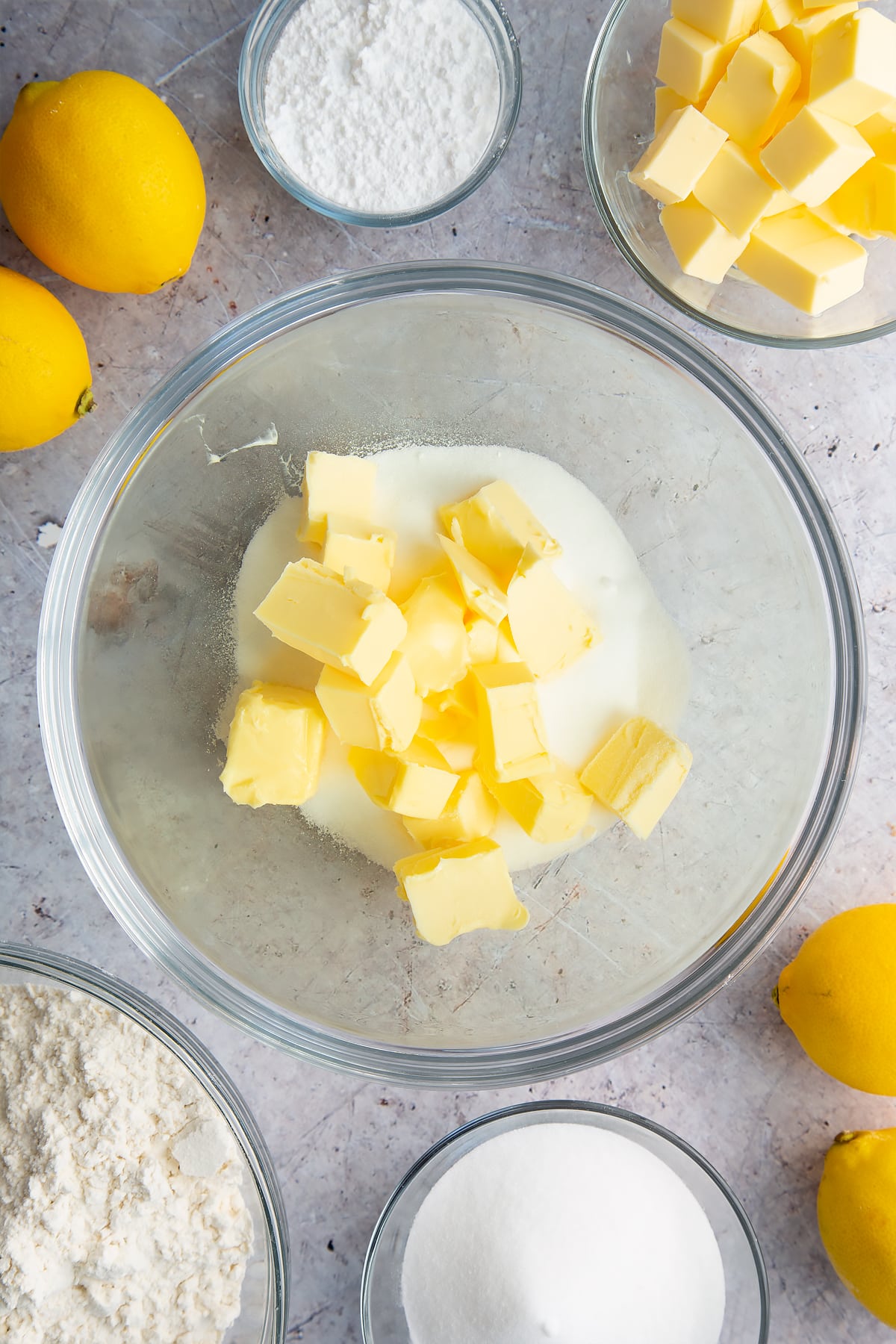 Butter and sugar in a glass bowl. Ingredients to make lemon drizzle cake surround the bowl. 