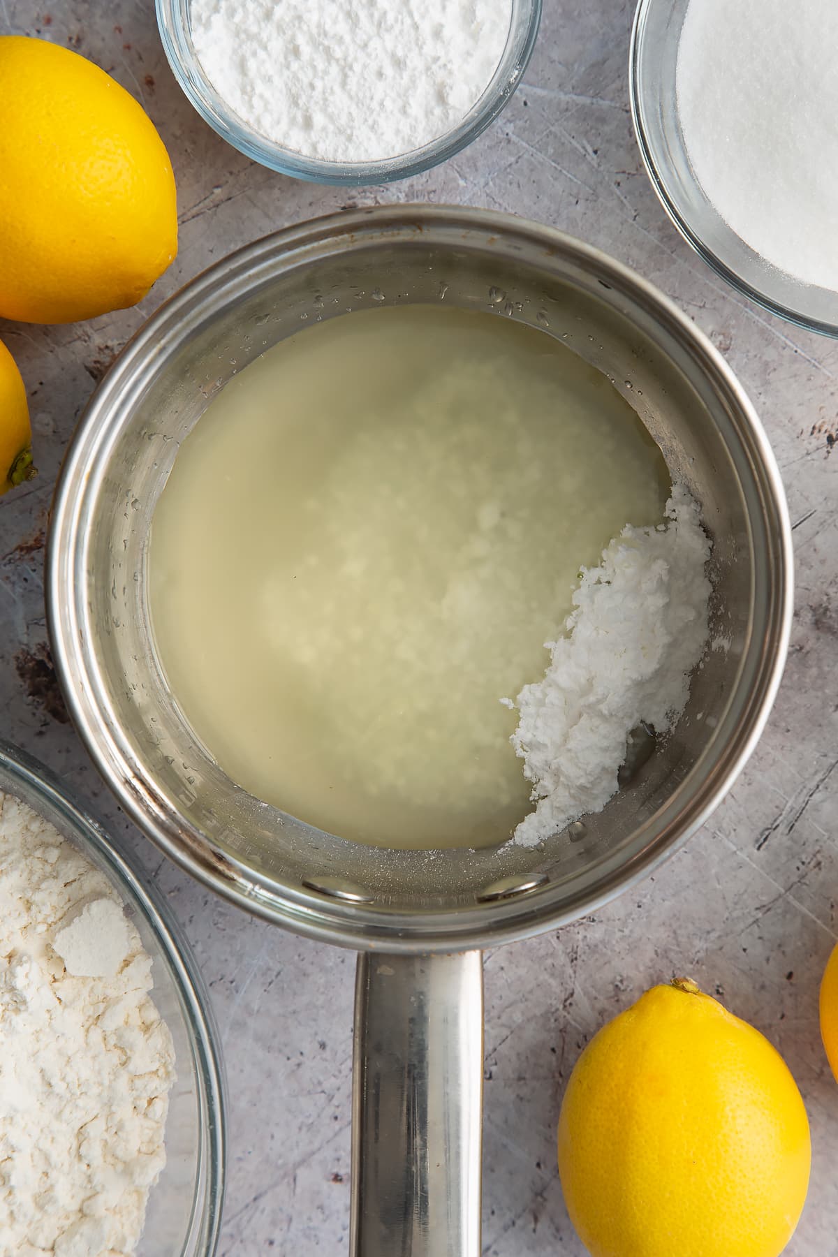 Lemon juice and icing sugar in a small metal pan. Ingredients to make lemon drizzle cake surround the pan. 