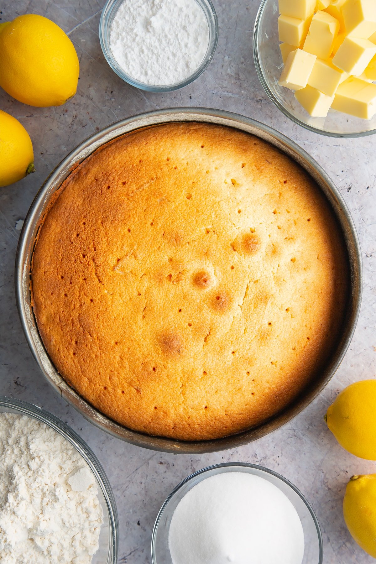 Freshly baked lemon drizzle cake in a cake tin. Holes have been poked in the top.