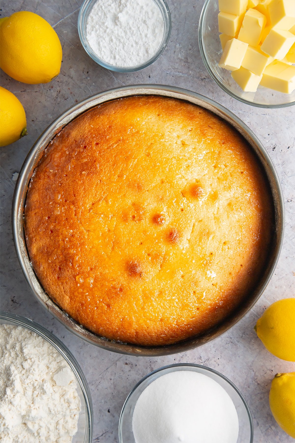 Freshly baked lemon drizzle cake in a cake tin. Holes have been poked in the top and lemon drizzle syrup has been poured on top.