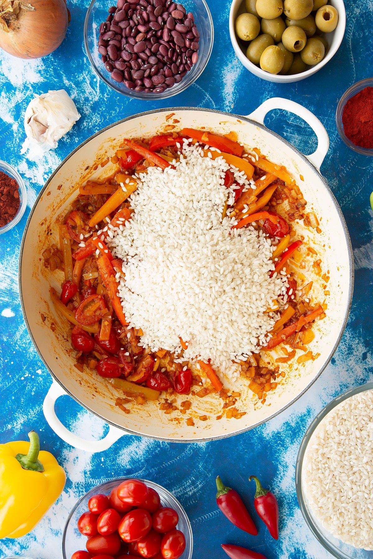 How do you say rice and beans in spanish 8 Sweated onions, spices, tomatoes and mixed sliced peppers in a pan with arborio rice on top. Ingredients to make easy Spanish rice and beans surround the pan.