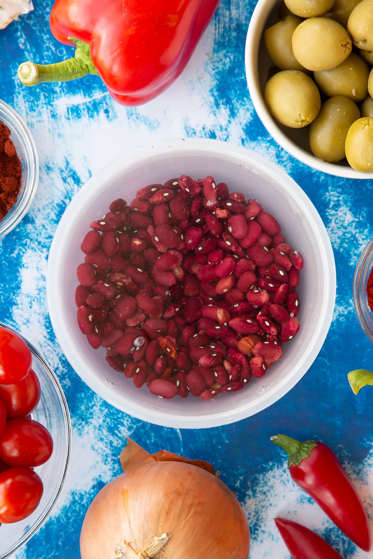 Dried kidney beans covered with water in a small pot. Ingredients to make easy Spanish rice and beans surround the pot.