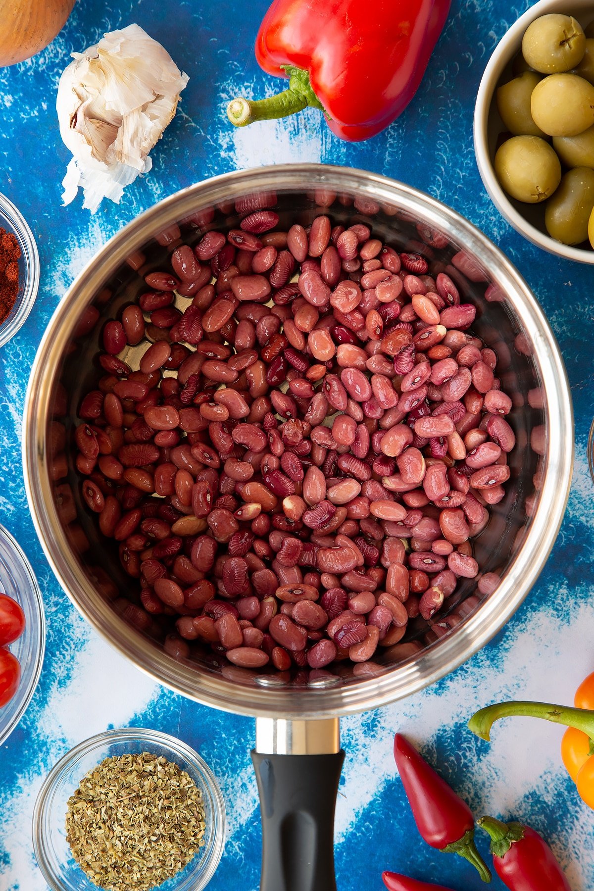 Soaked kidney beans in a saucepan. Ingredients to make easy Spanish rice and beans surround the pan.