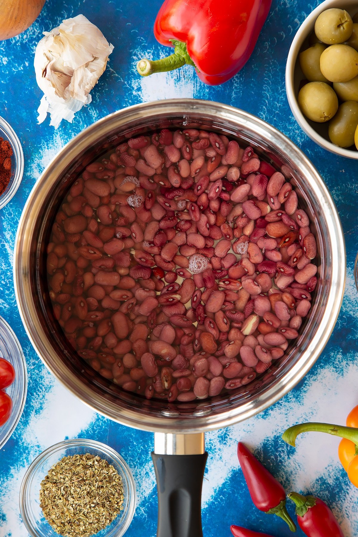 Soaked kidney beans covered with water in a saucepan. Ingredients to make easy Spanish rice and beans surround the pan.