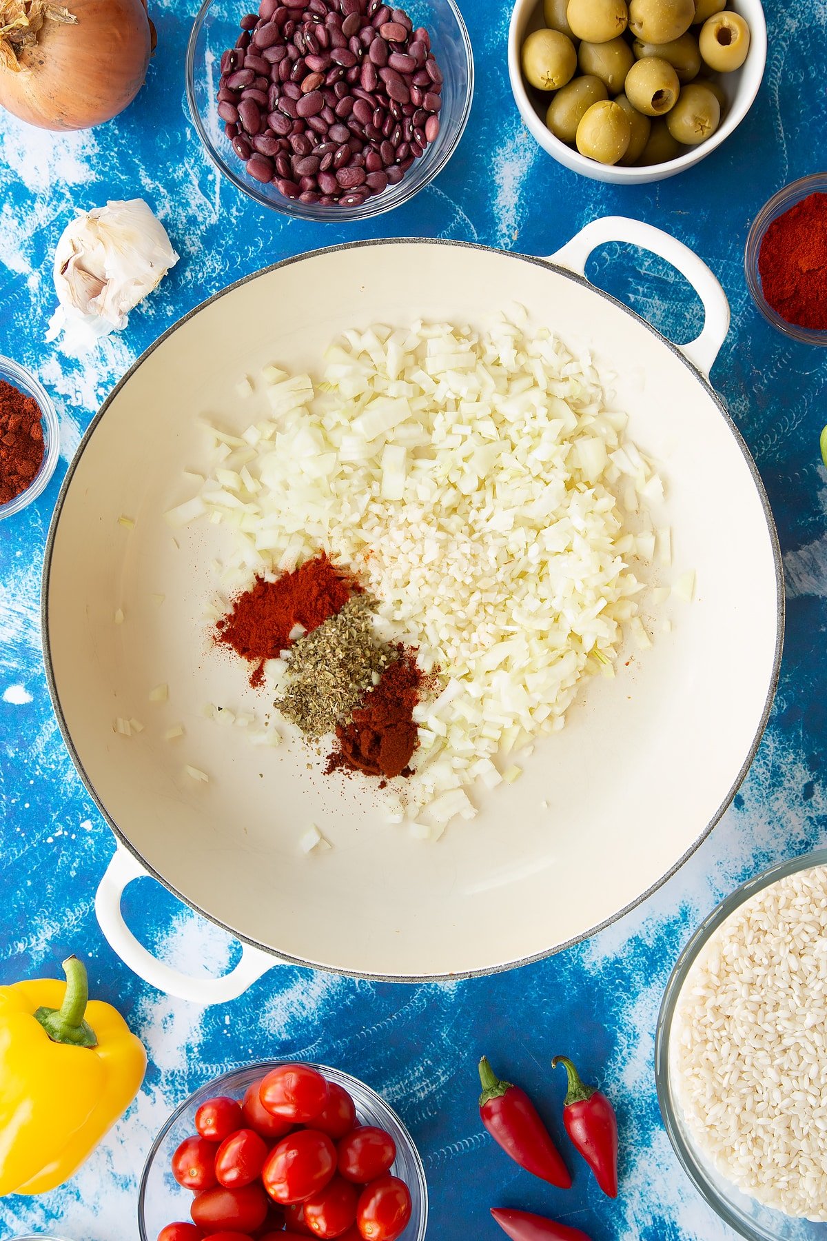 Chopped onions, garlic, cayenne, paprika and oregano in a pan. Ingredients to make easy Spanish rice and beans surround the pan.