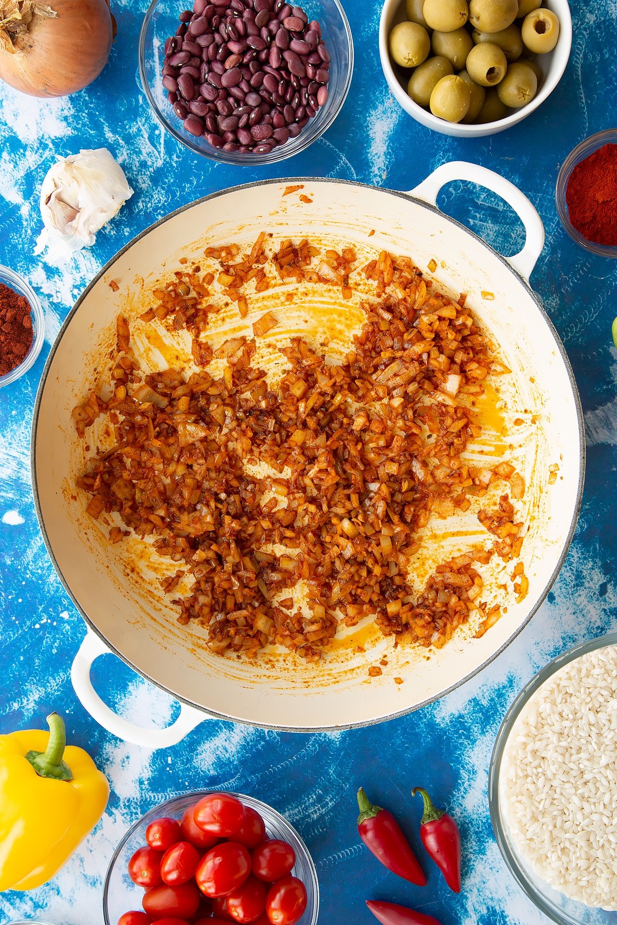 Sweated onions, garlic, cayenne, paprika and oregano in a pan. Ingredients to make easy Spanish rice and beans surround the pan.