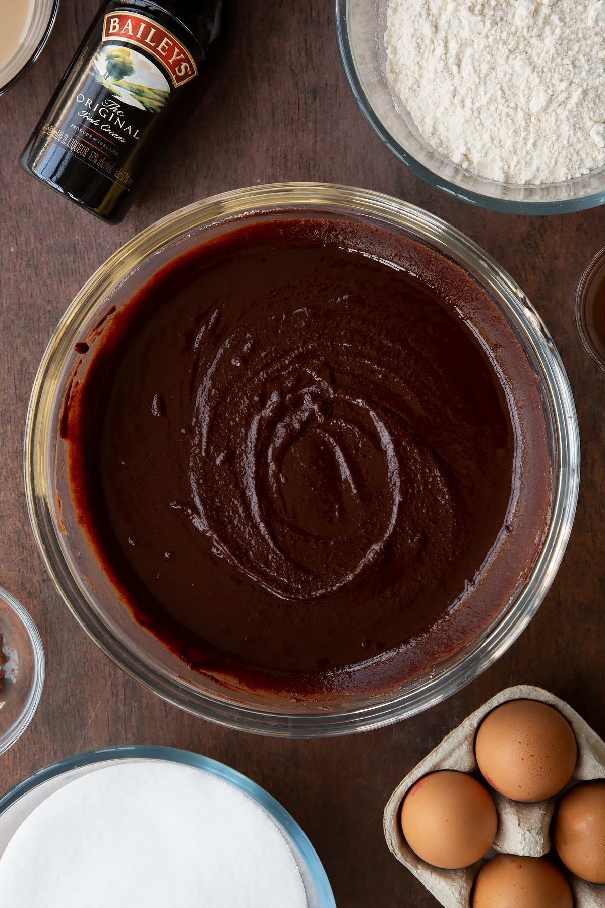 Melted chocolate, butter and sugar in a glass bowl. Ingredients to make Baileys brownies surround the bowl.