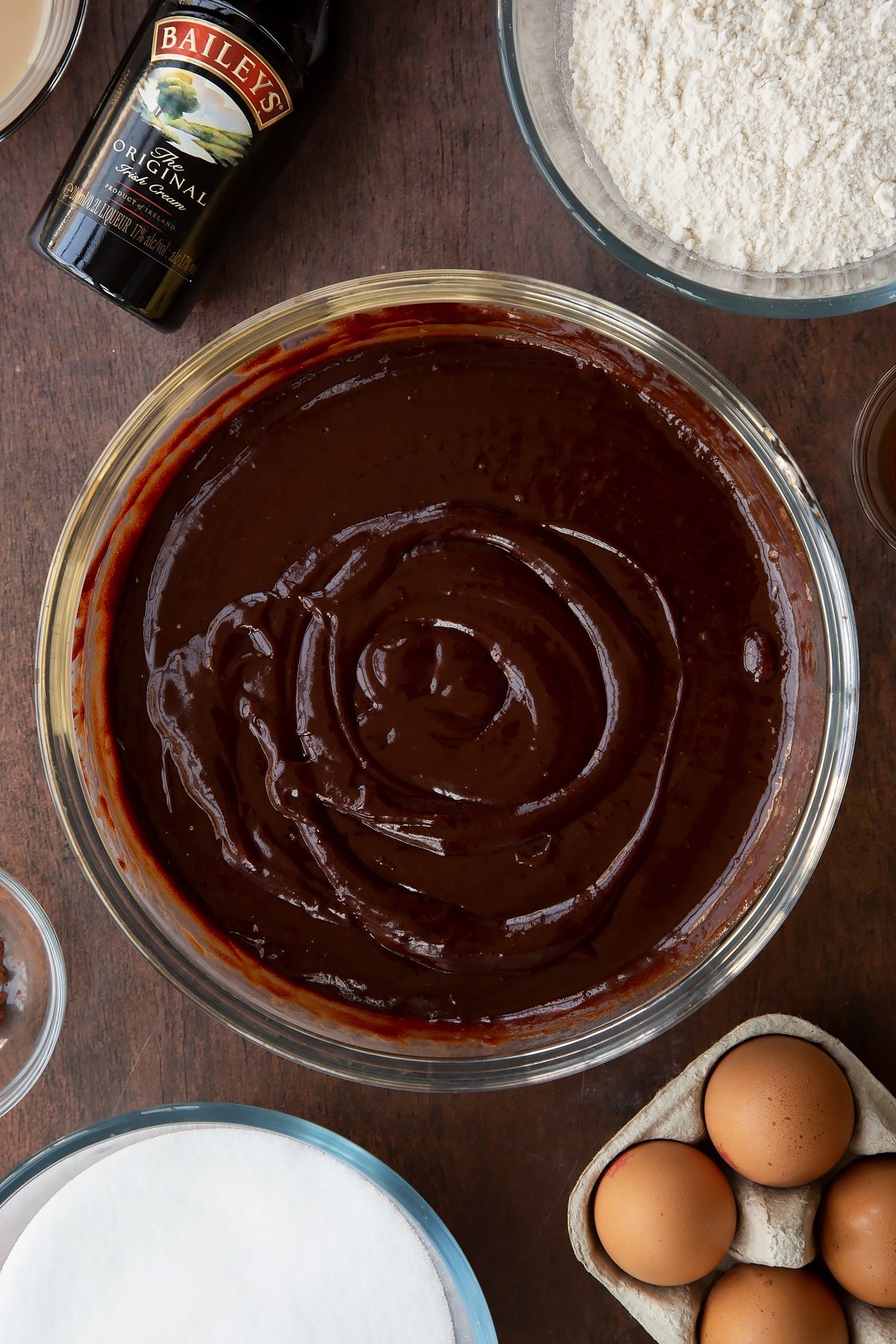 Melted chocolate, butter, Baileys, sugar and eggs in a glass bowl. Ingredients to make Baileys brownies surround the bowl.