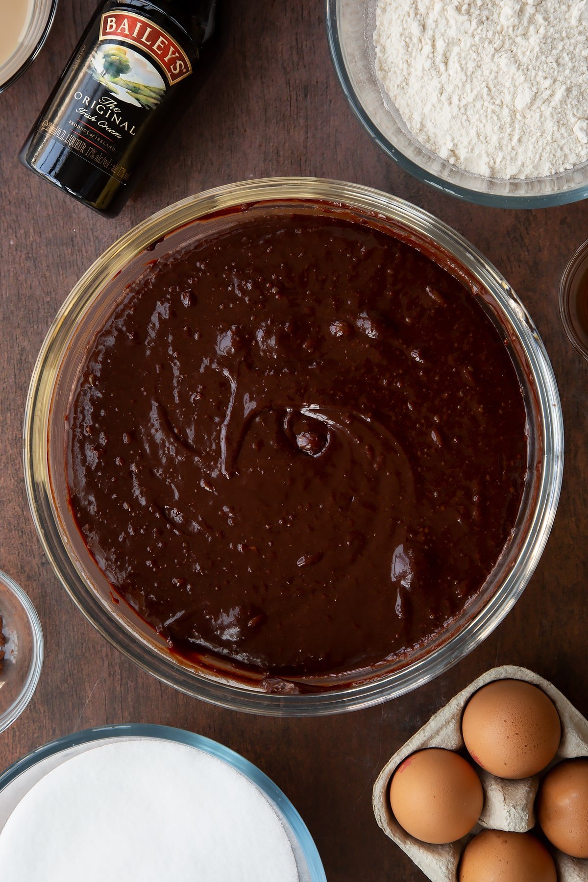 Baileys brownie batter in a glass bowl. Ingredients to make Baileys brownies surround the bowl.