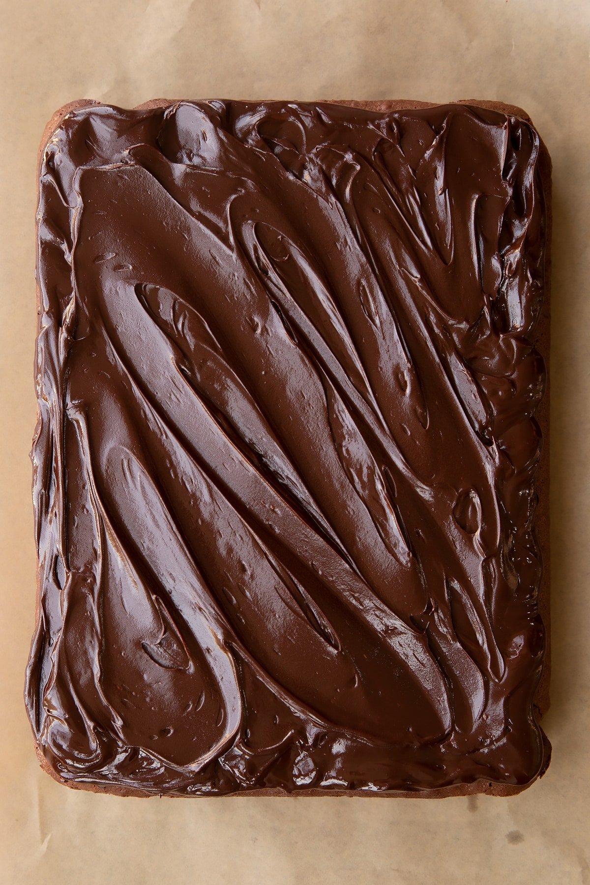 Baked candy cane brownie on baking paper with dark chocolate ganache spread on top.