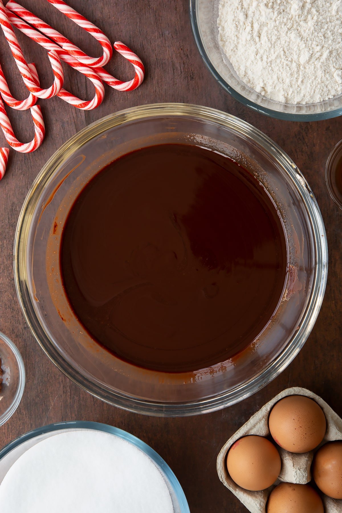 Melted butter and dark chocolate in a glass bowl. Ingredients to make Candy cane brownies surround the bowl.