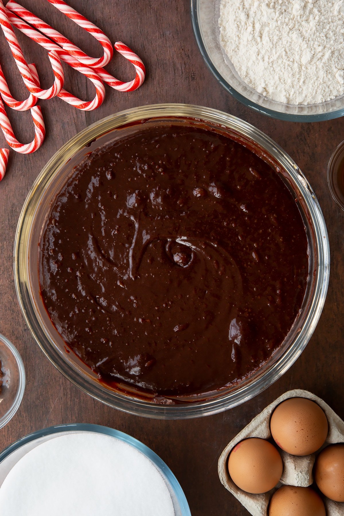 Brownie batter in a glass bowl. Ingredients to make Candy cane brownies surround the bowl.