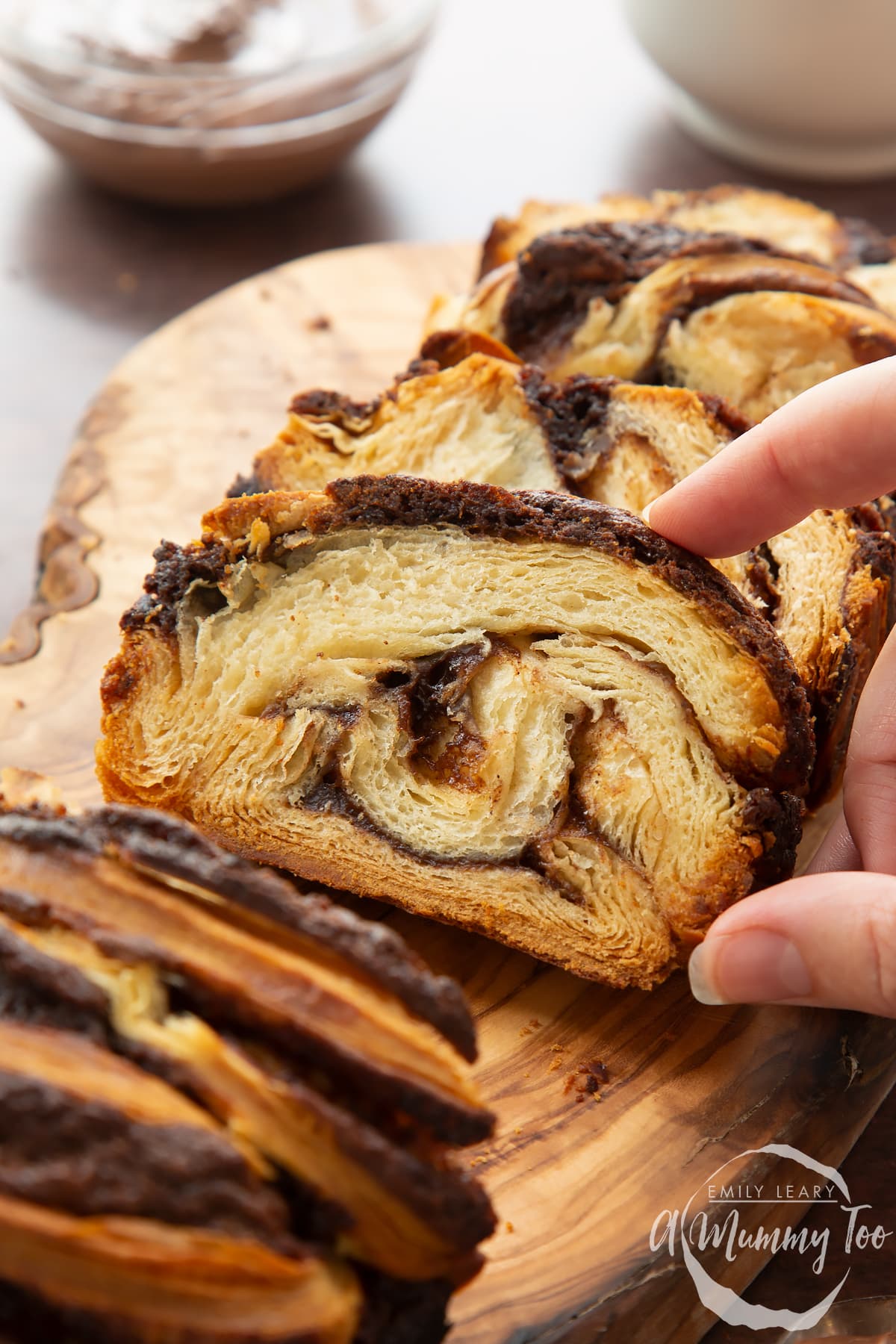 Hand reaching for a slice of cinnamon swirl babka on a wooden board.