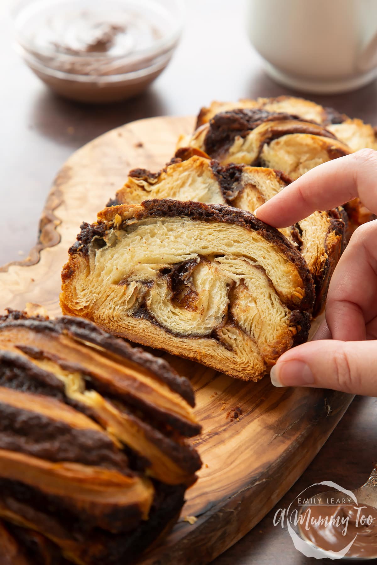 Slices of cinnamon swirl babka on a wooden board. A hand reaches for one.