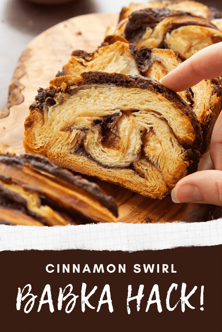 Hand reaching for a slice of cinnamon swirl babka on a wooden board. Caption reads: cinnamon swirl babka hack!