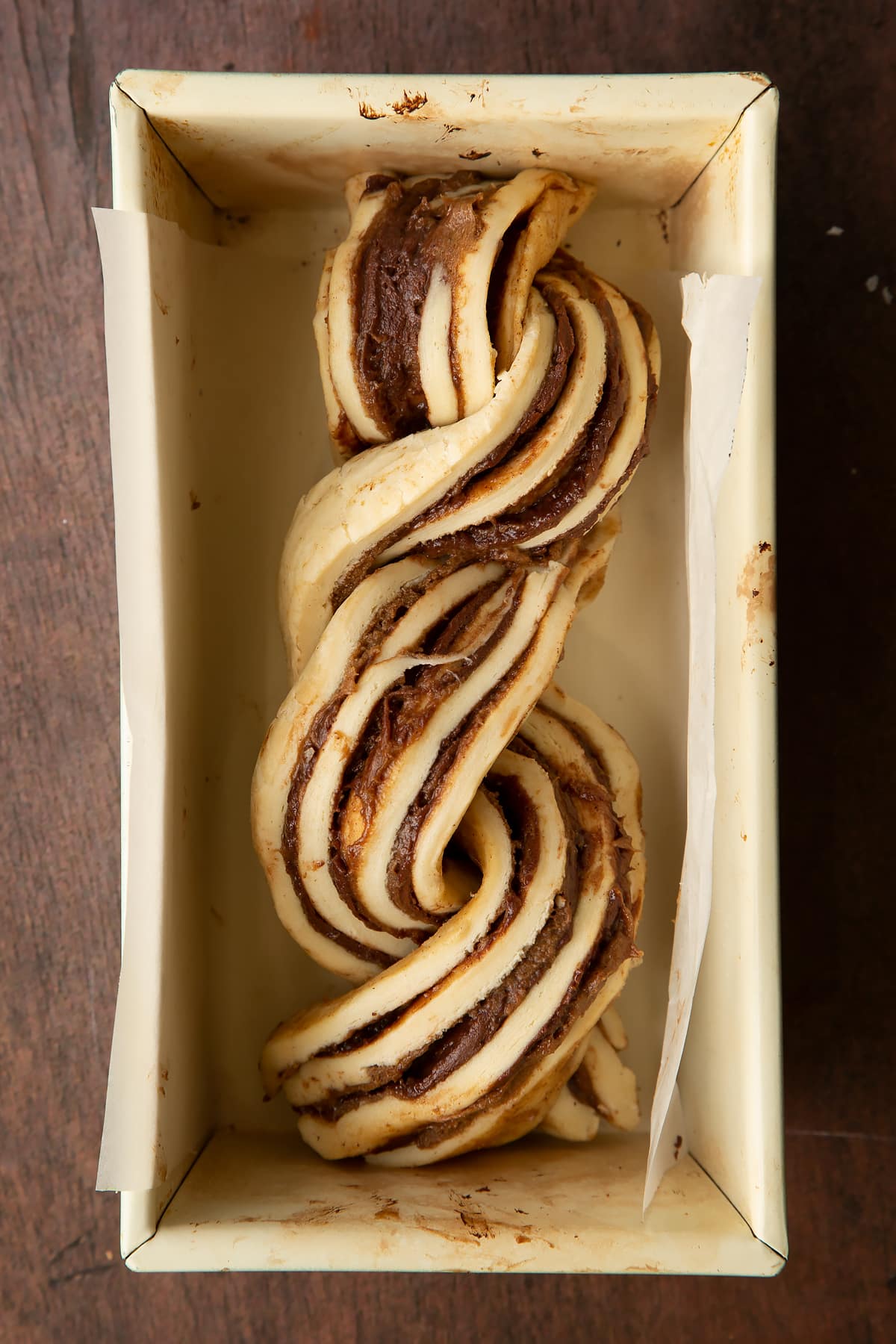 Twisted cinnamon swirl babka dough in a lined baking tin.