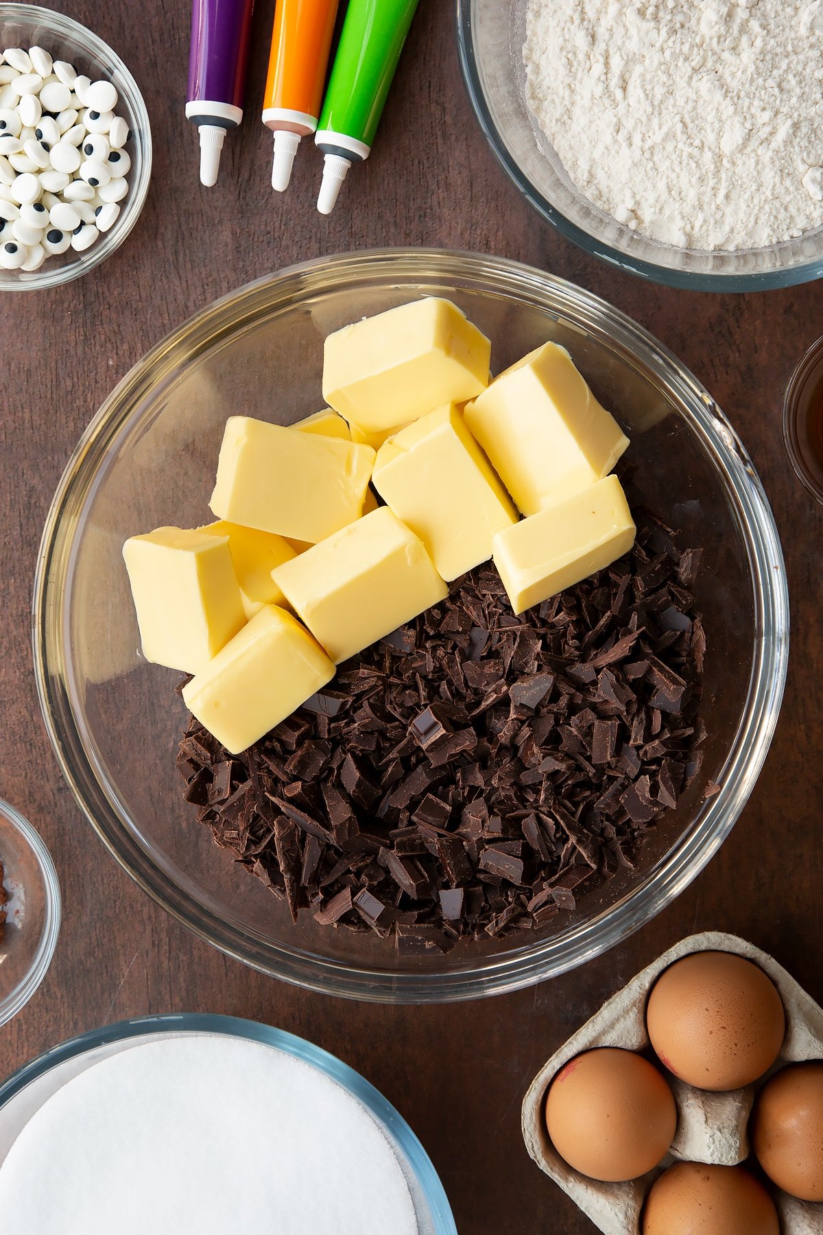 Butter and chopped dark chocolate in a glass bowl. Ingredients to make Halloween brownies surround the bowl.