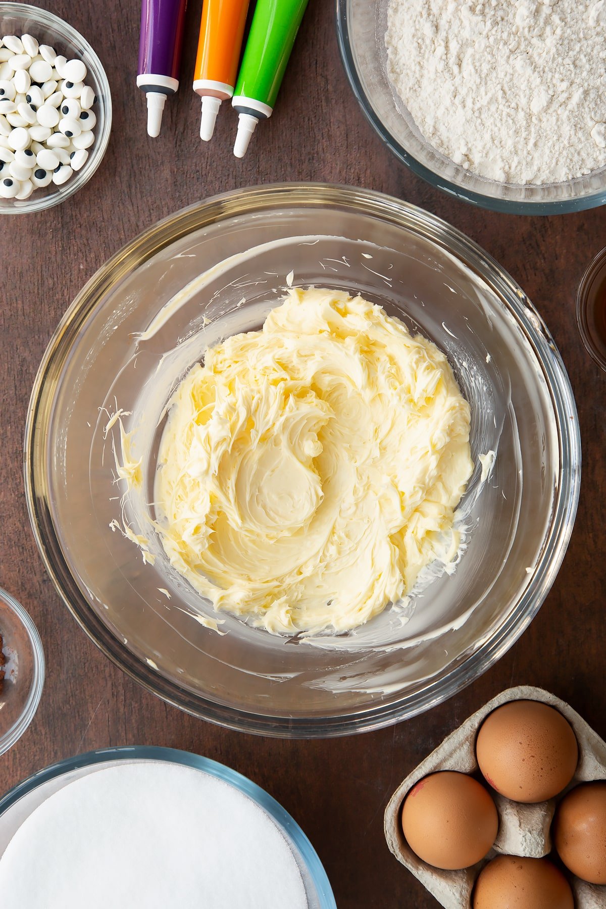 Whipped butter in a glass bowl. Ingredients to make Halloween brownies surround the bowl.