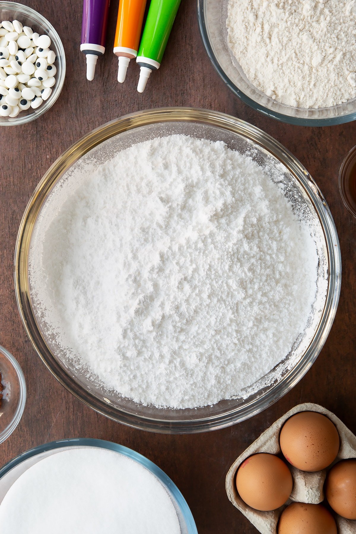 Whipped butter in a glass bowl with icing sugar on top. Ingredients to make Halloween brownies surround the bowl.