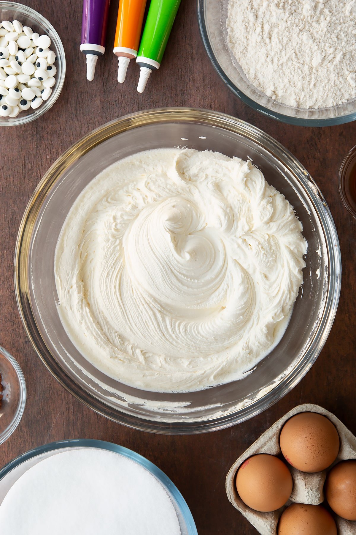 Frosting in a glass bowl. Ingredients to make Halloween brownies surround the bowl.