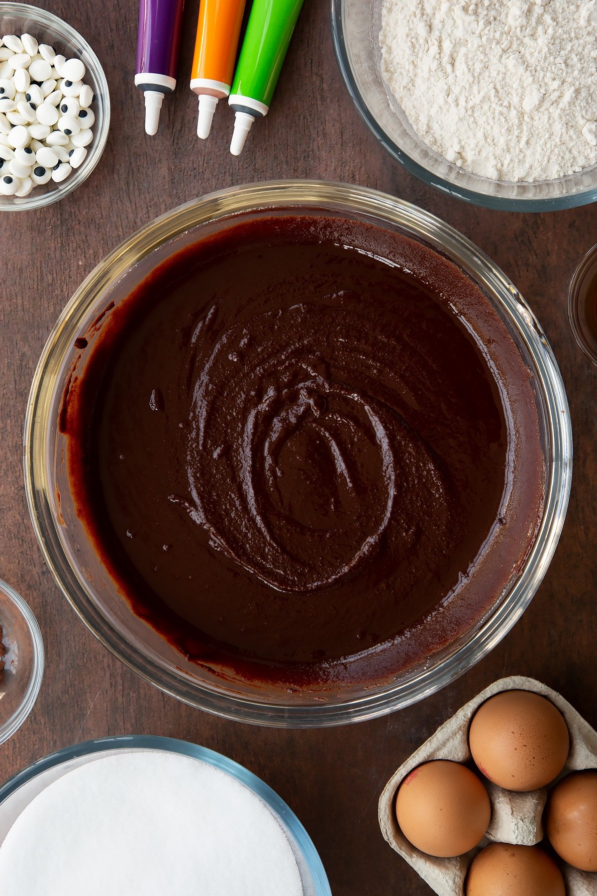 Melted butter, dark chocolate and sugar in a glass bowl. Ingredients to make Halloween brownies surround the bowl.