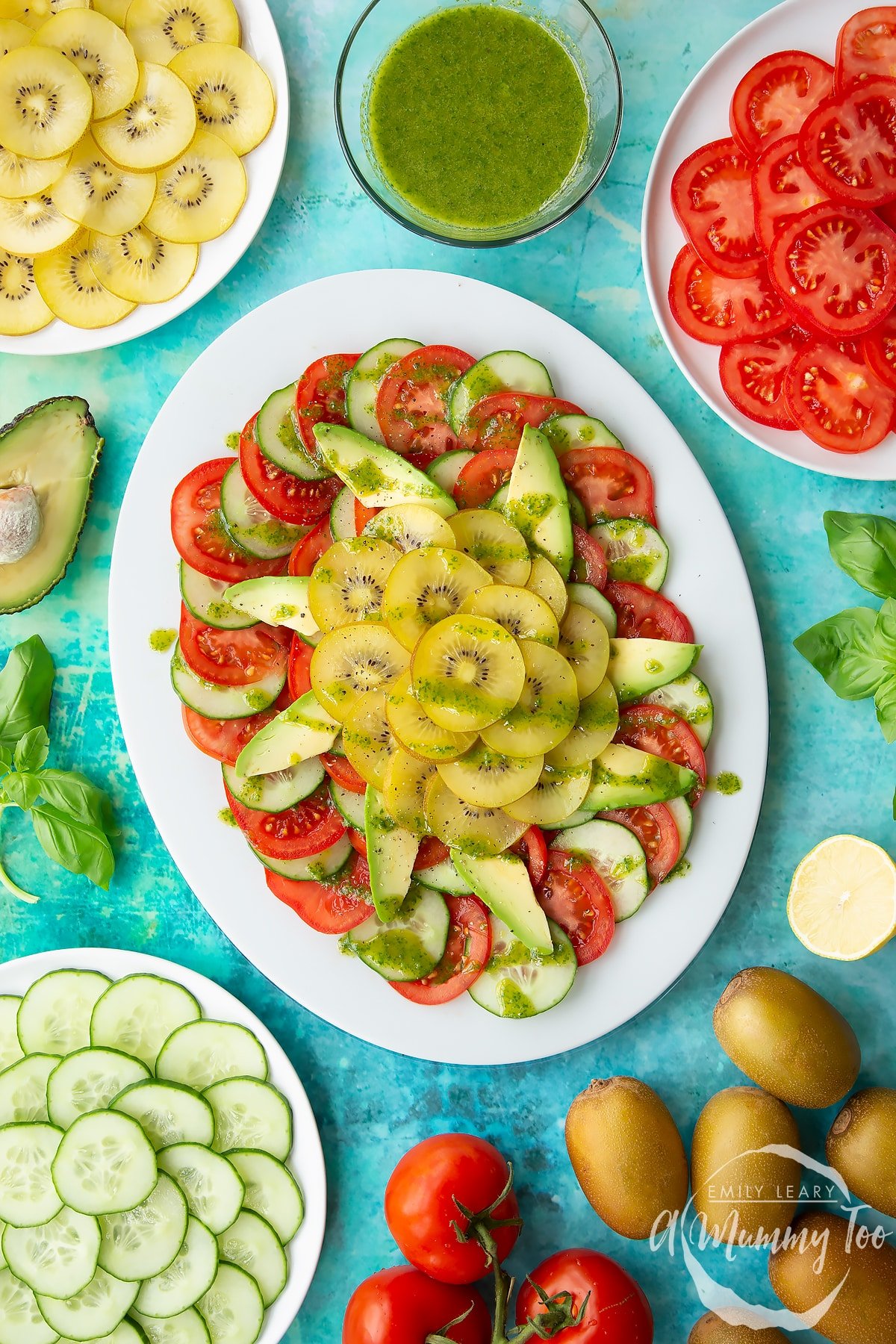 Kiwi salad with basil oil on an oval white platter, surrounded by ingredients.