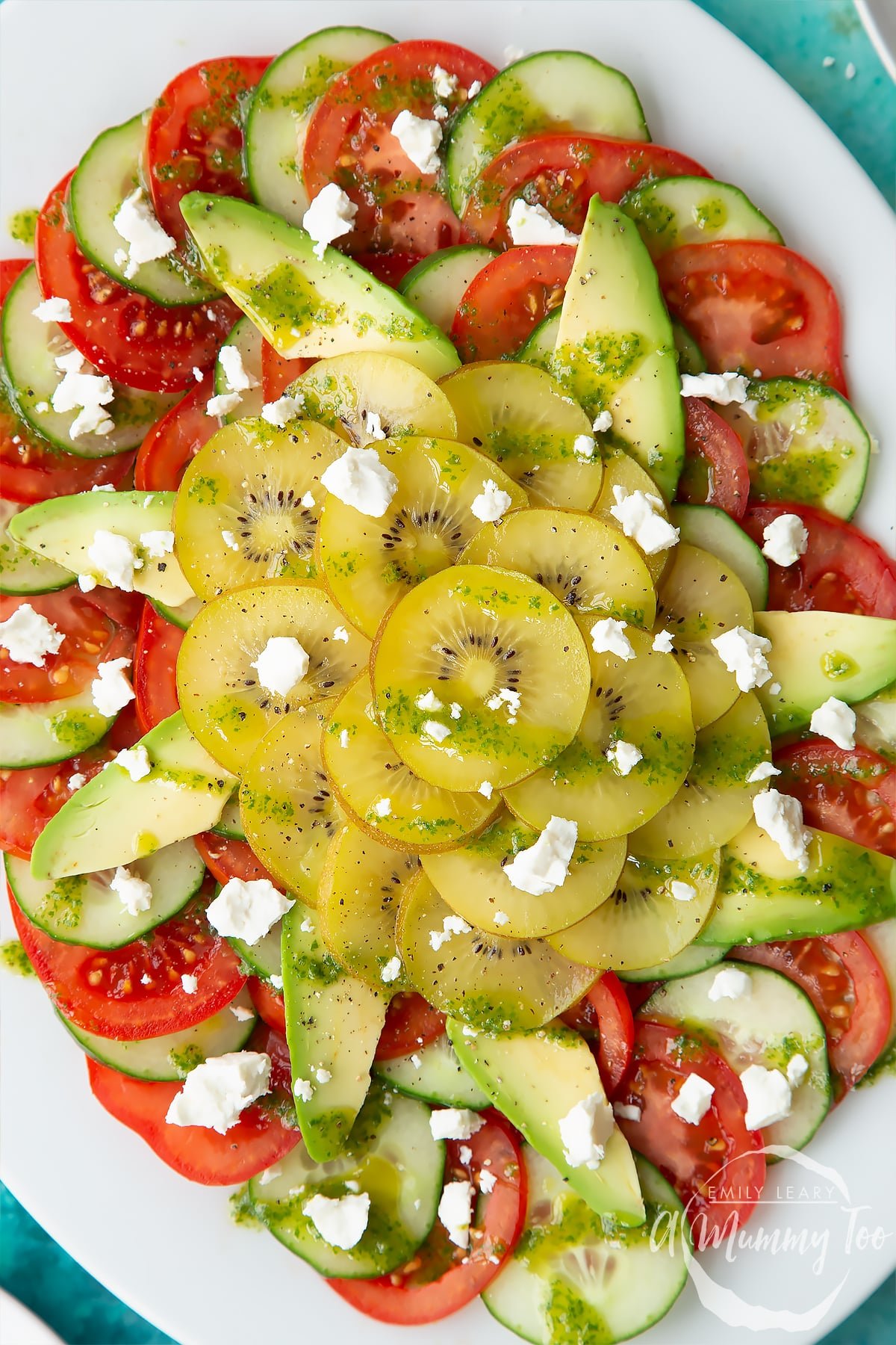 Close up of kiwi feta salad with basil oil on an oval white platter.