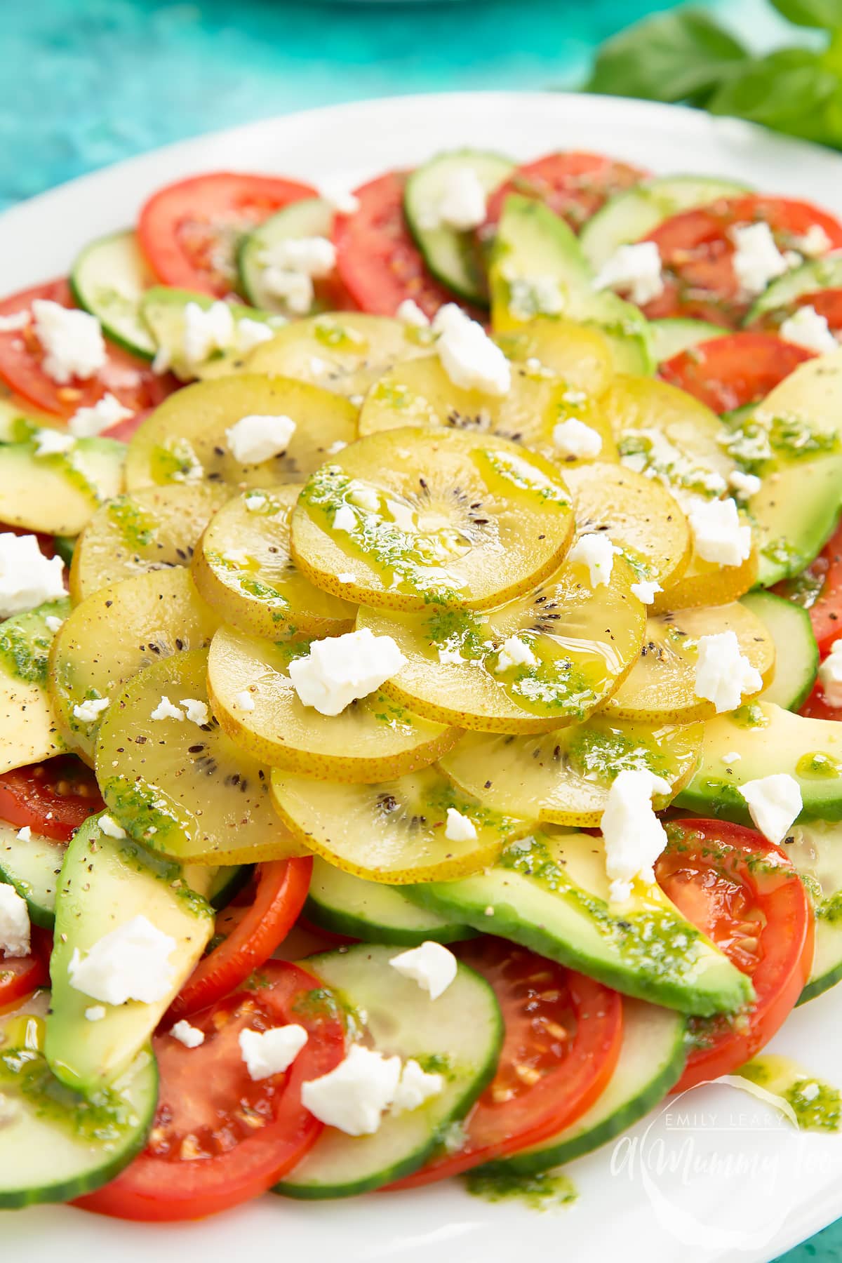 Close up of kiwi feta salad with basil oil on a white platter.