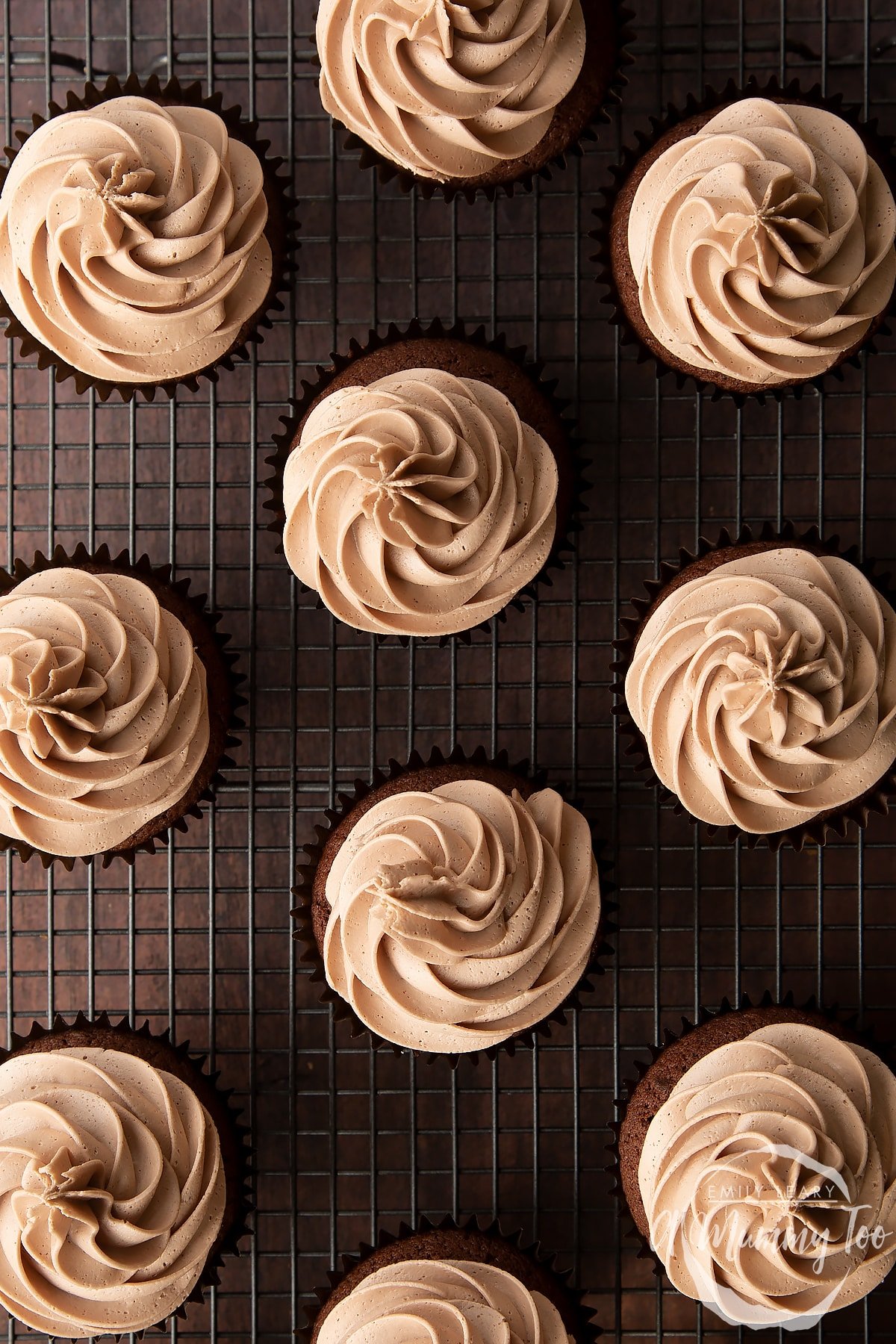 Baileys icing piped onto a chocolate cupcakes on a wire cooling rack.