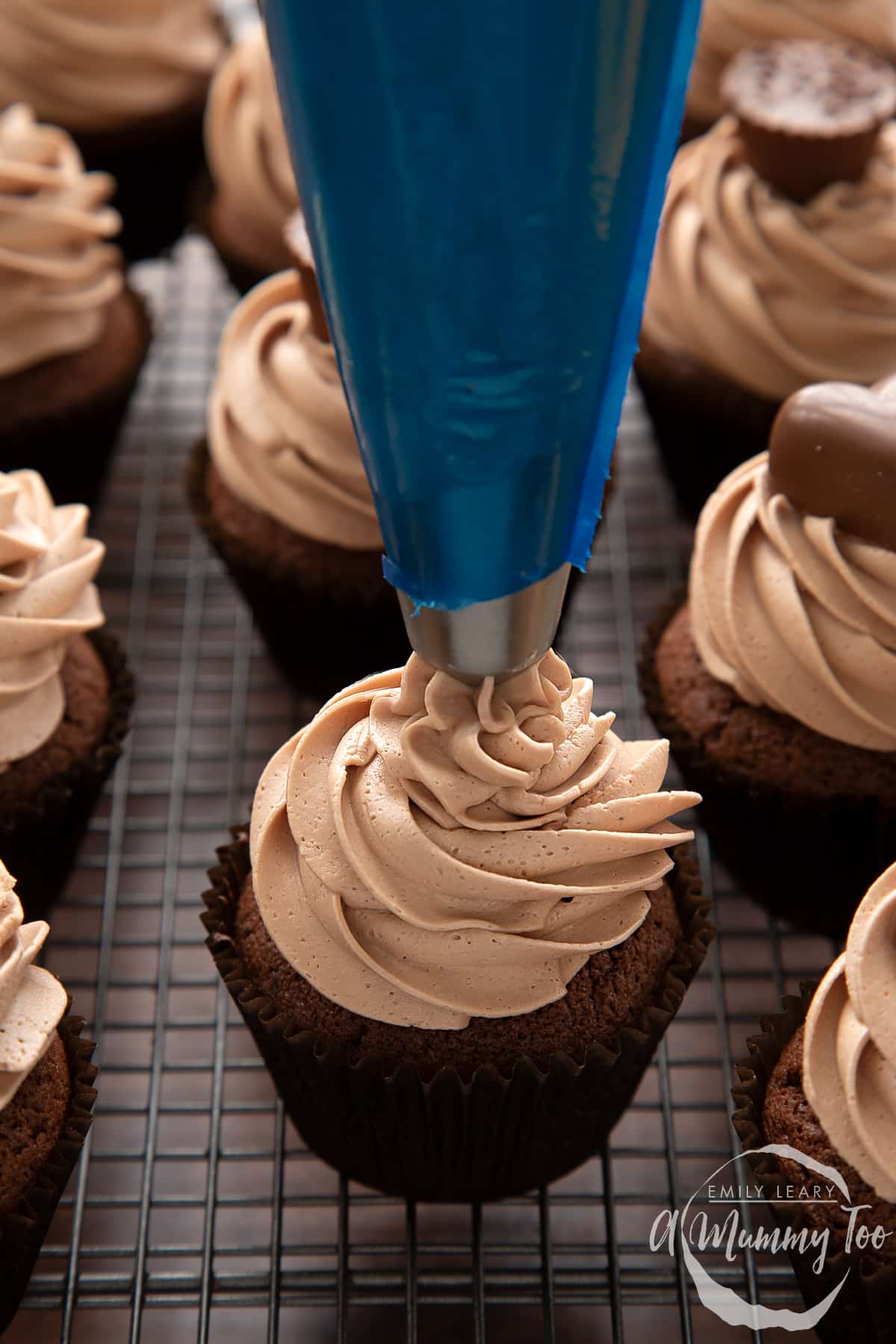 Baileys icing being piped onto a chocolate cupcake using a blue piping bag with a metal star nozzle.