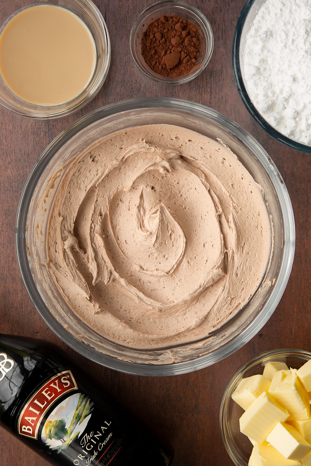 Baileys icing in a glass bowl. Ingredients to make Baileys icing surround the bowl.