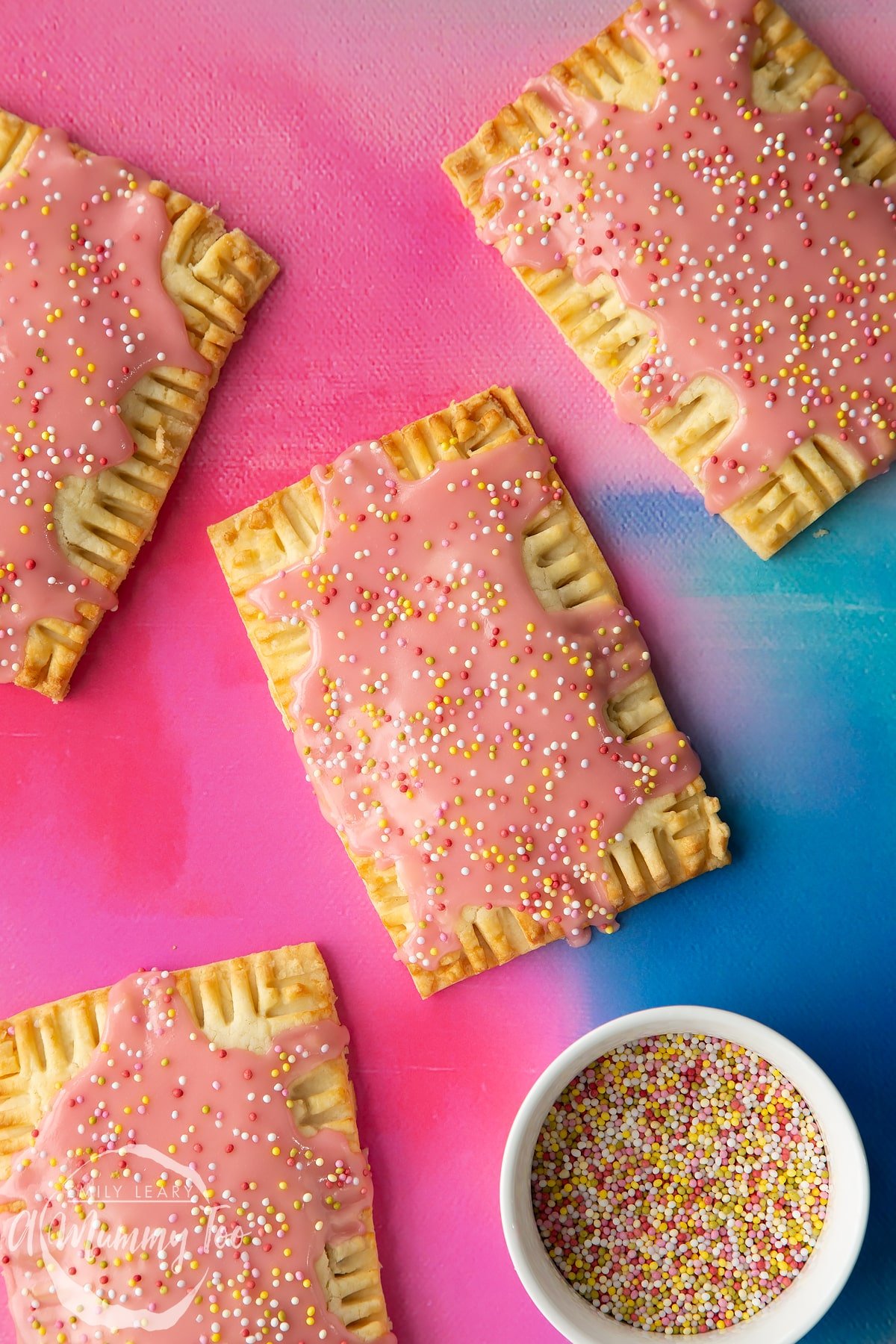 Gluten free pop tarts with pink icing and pastel sprinkles on a bright pink and blue backdrop.