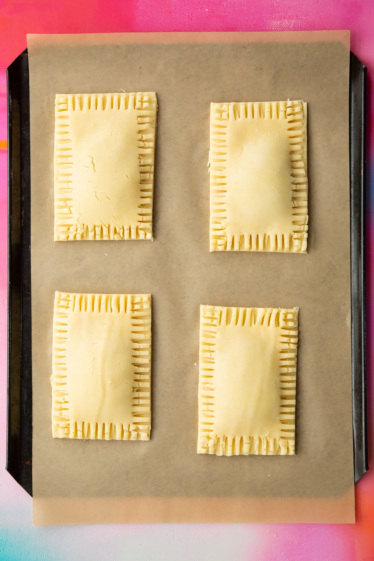 Four raw gluten free pop tarts on baking tray lined with baking paper. The edges have been crimped and neatened.