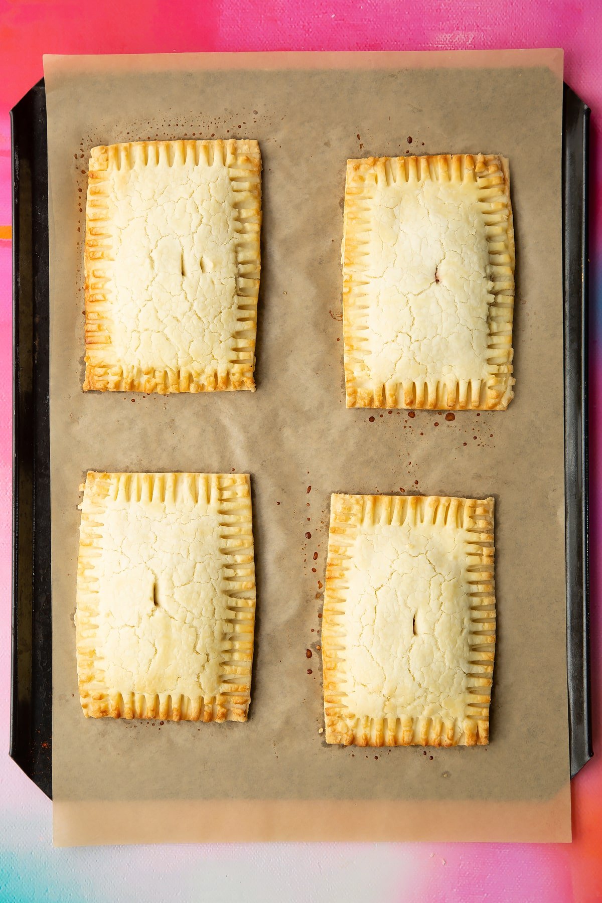 Four freshly baked gluten free pop tarts on a baking tray lined with baking paper. 