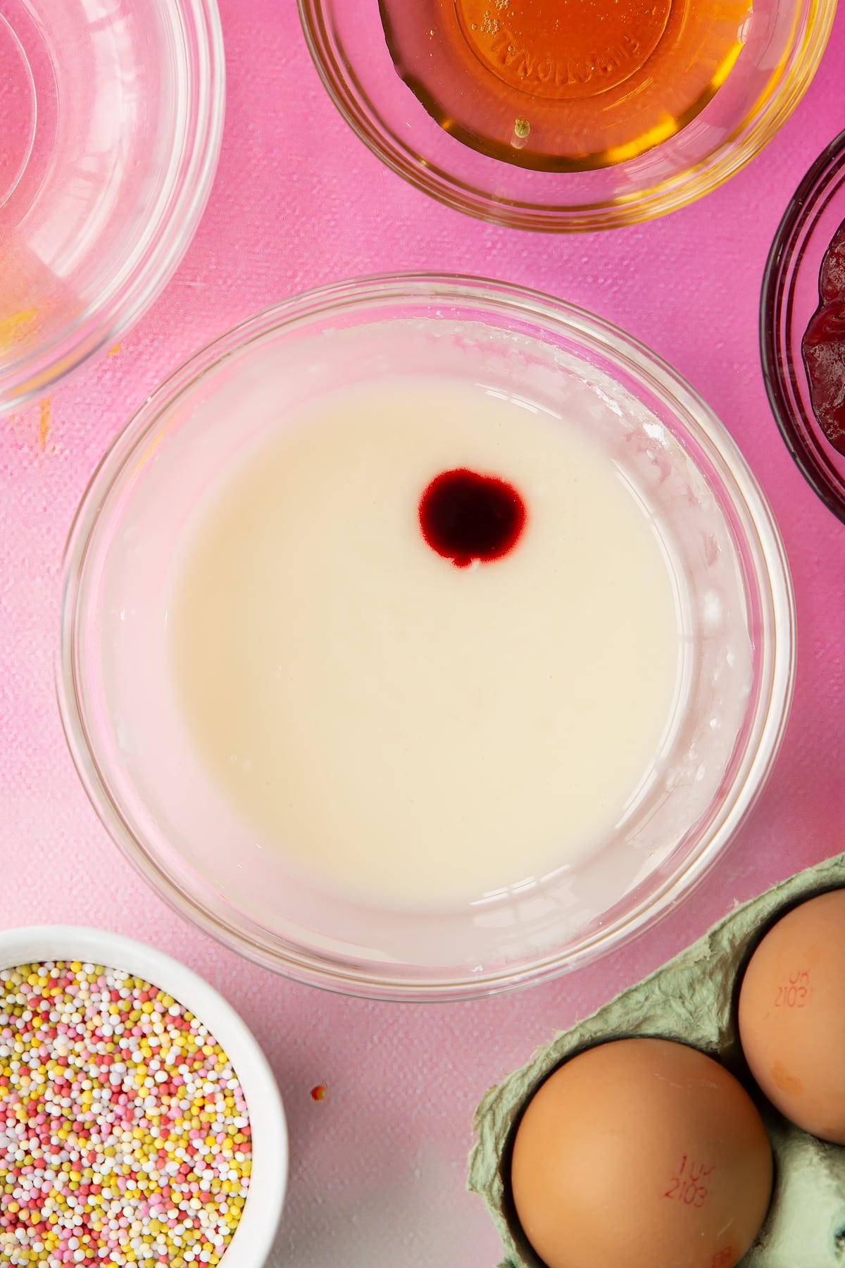 White icing in a small bowl with a drop of red food colouring. Ingredients to make gluten free pop tarts surround the bowl.