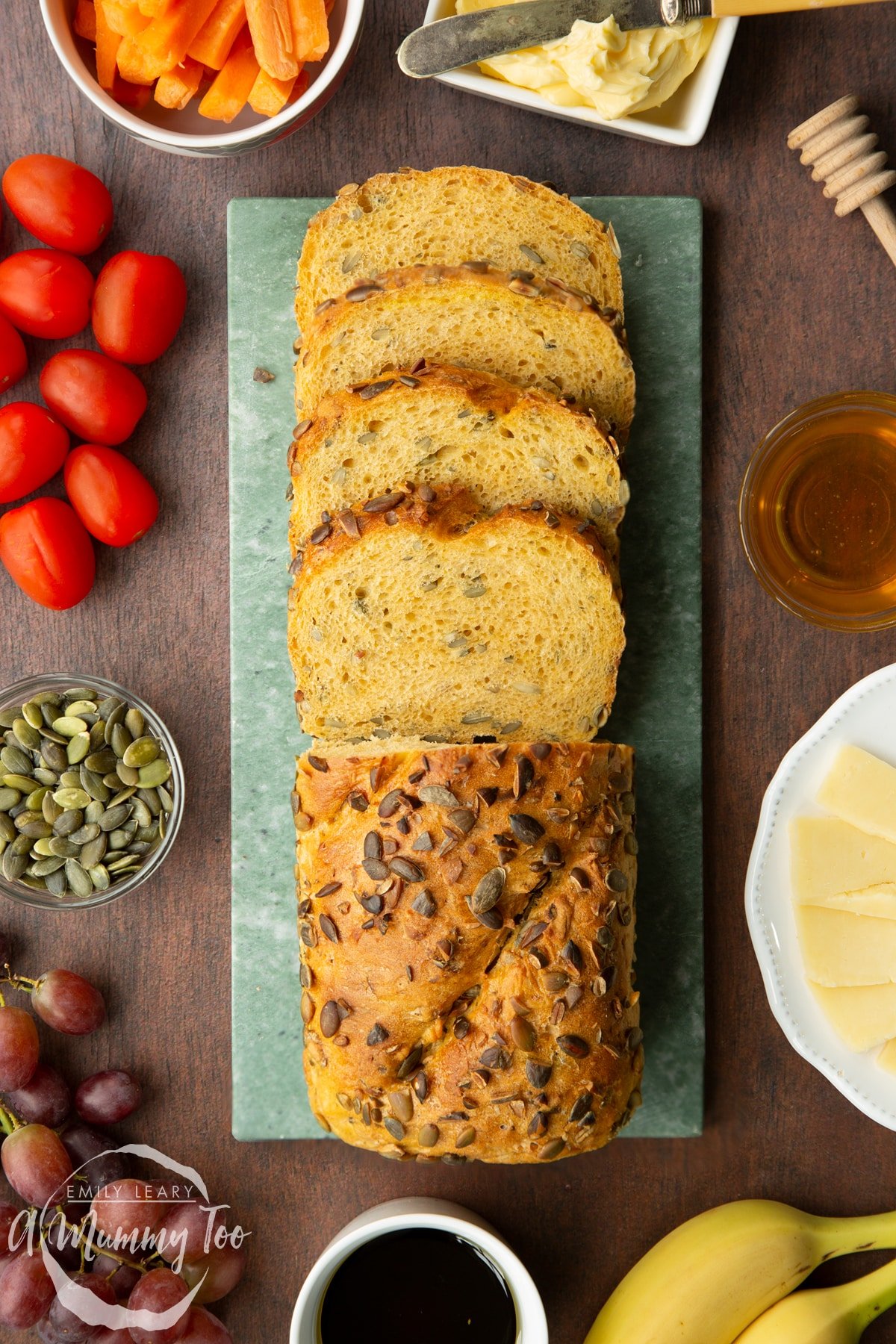 A pumpkin seed bread loaf on a marble board. Half of the loaf has been cut into slices.