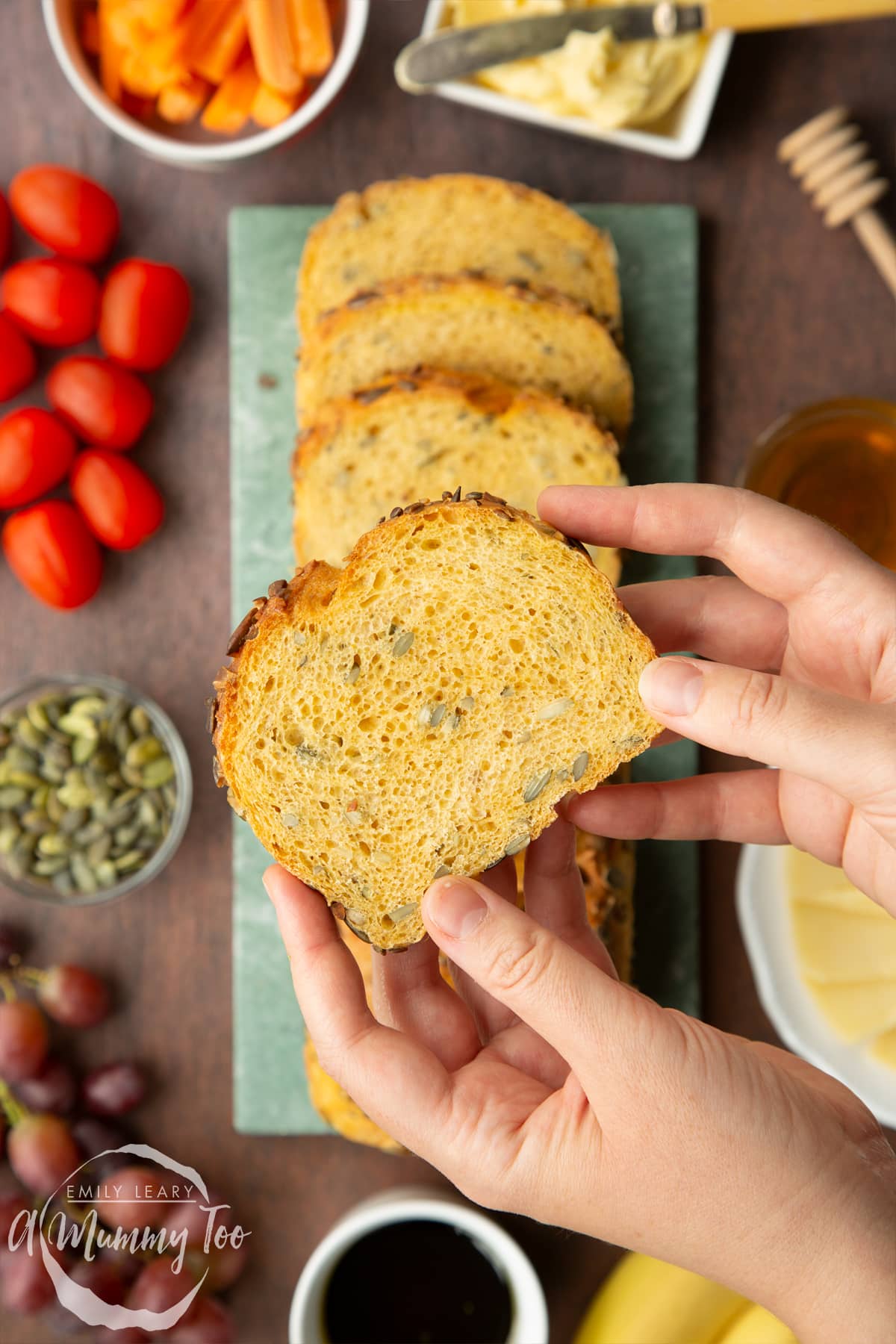 Hand holding a slice of pumpkin seed bread above a more of the loaf.