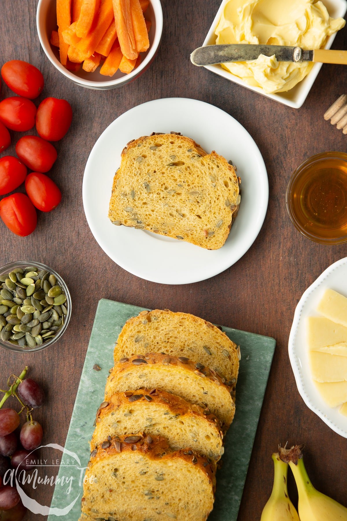 A slice of pumpkin seed bread on a white plate. More slices are on a marble board.