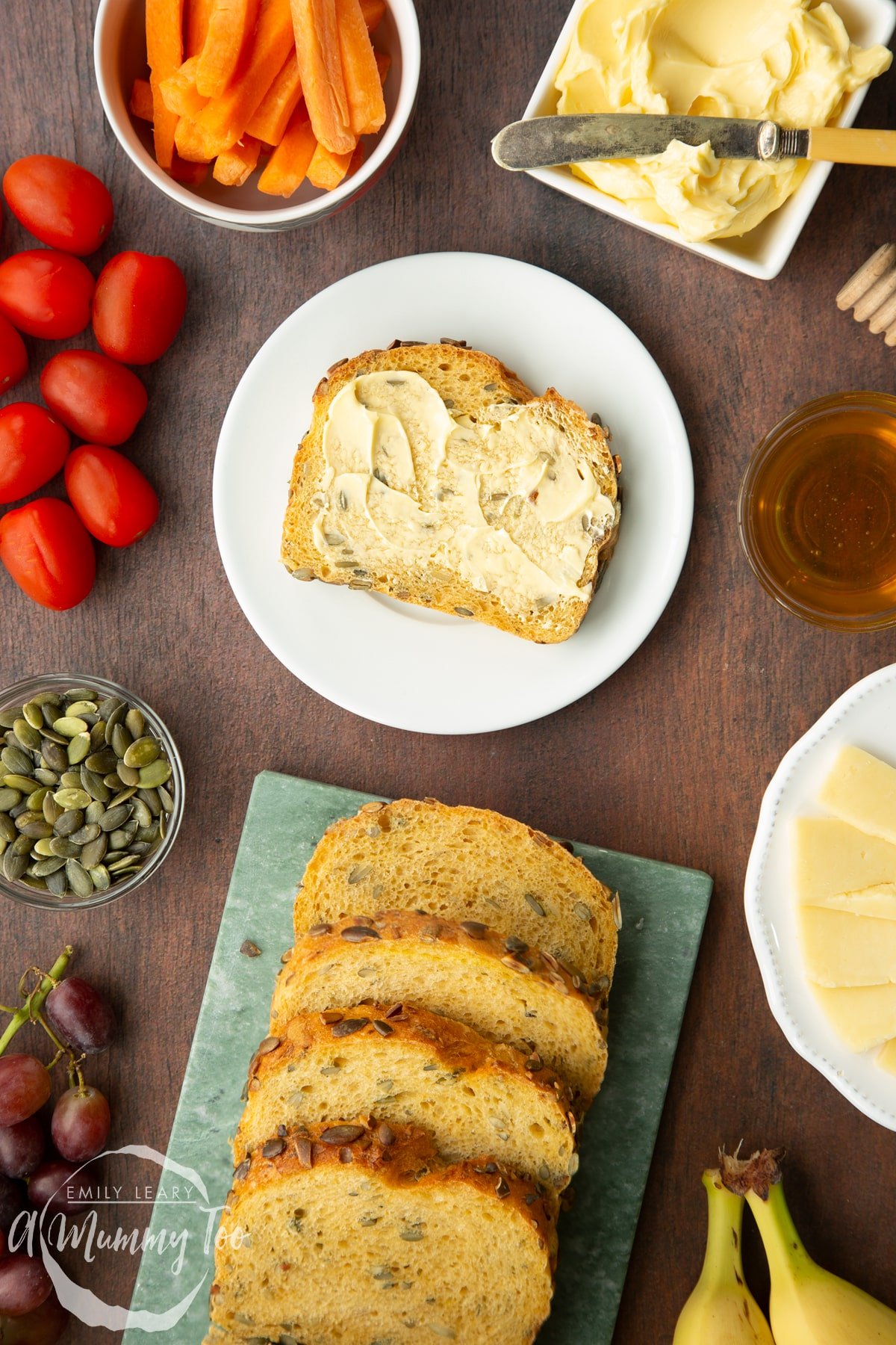 A buttered slice of pumpkin seed bread on a white plate. More slices are on a marble board.