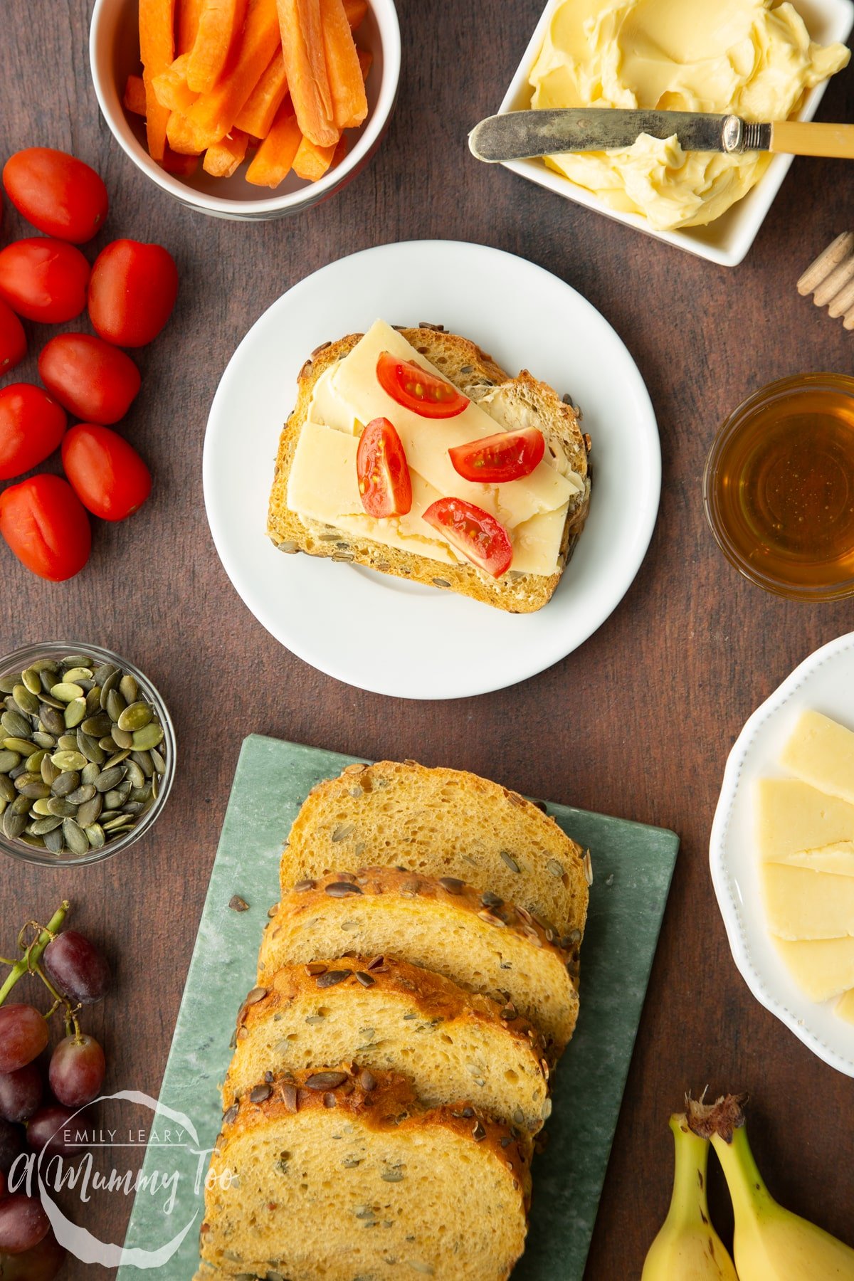 A slice of pumpkin seed specie topped with cheese and tomatoes on a white plate. Increasingly slices are on a marble board.