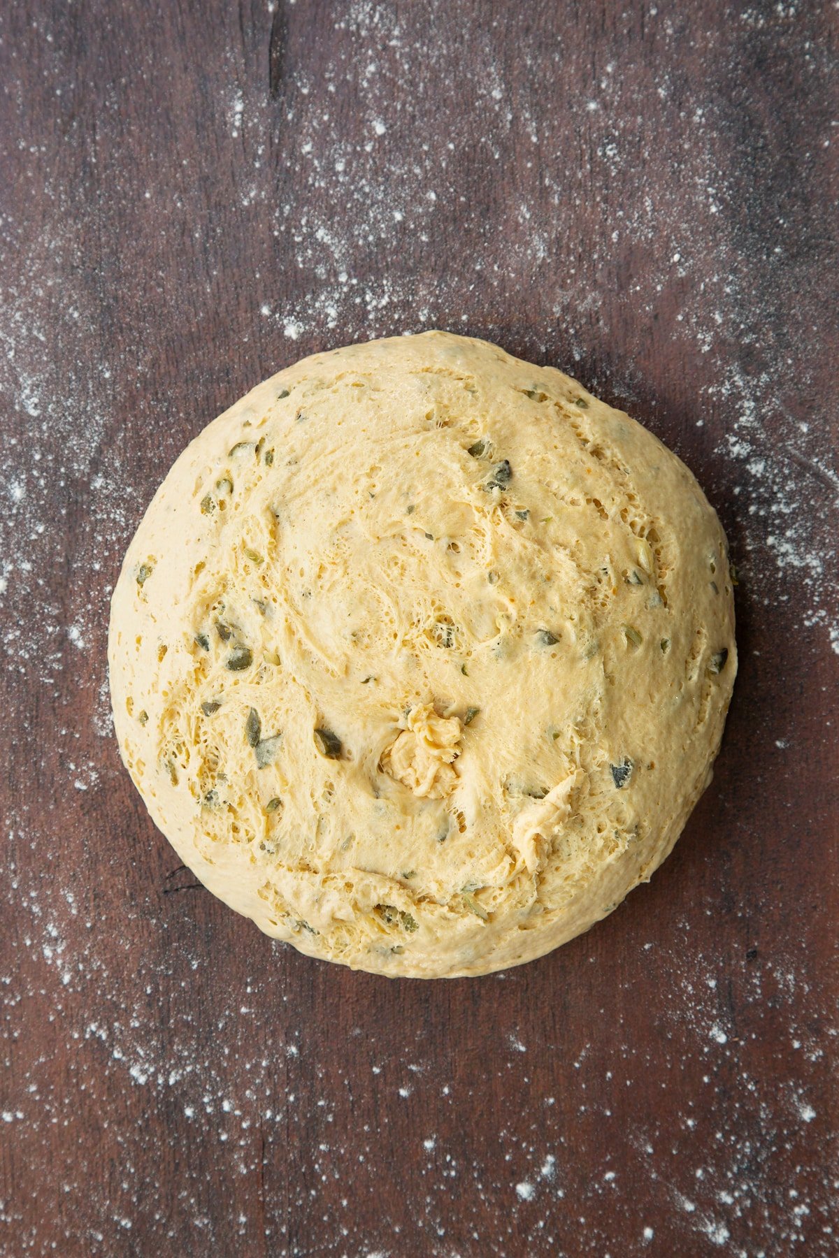 A large ball of proved pumpkin seed bread dough turned out onto a floured surface.