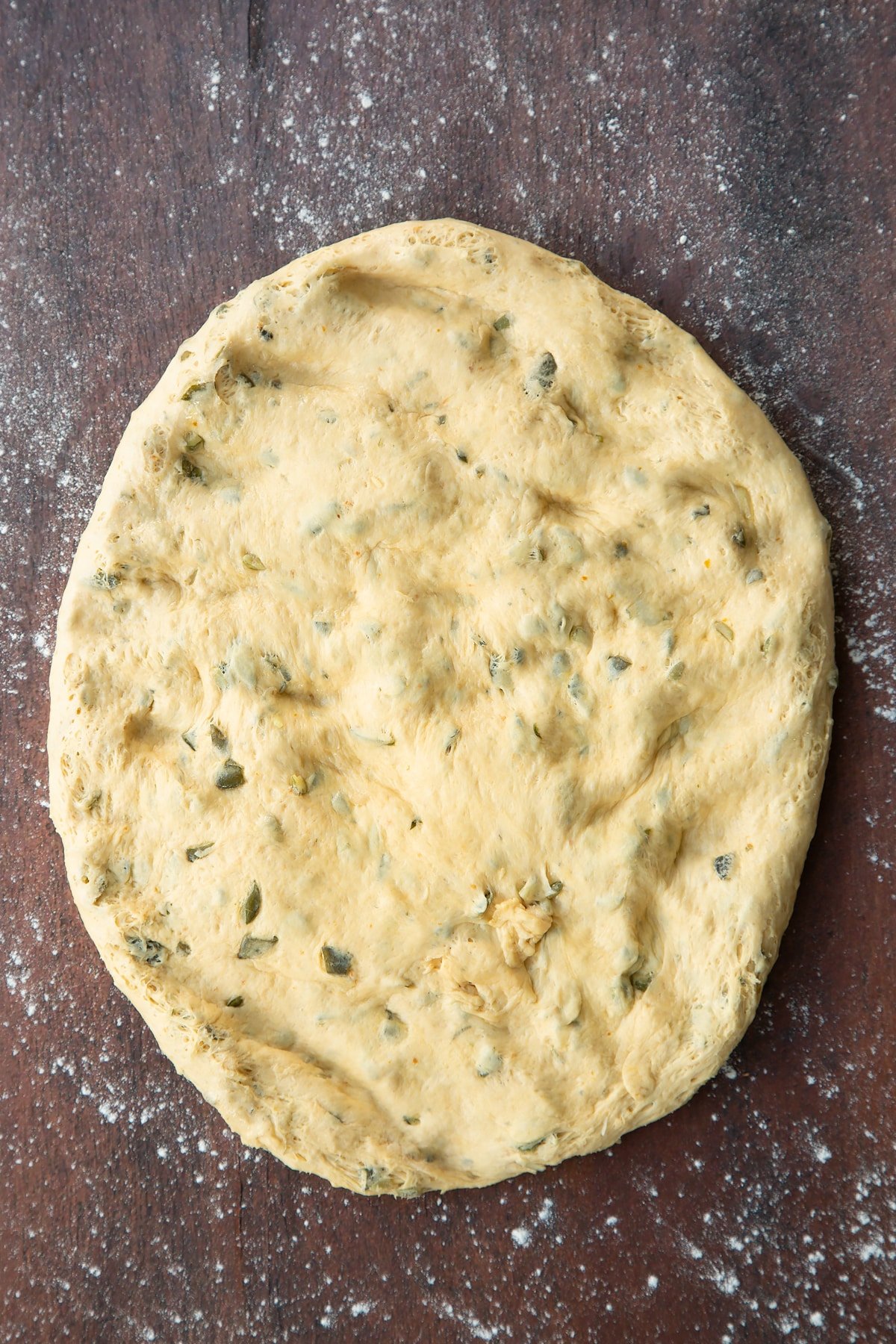 Pumpkin seed bread dough pressed into a flat oval on a floured surface.