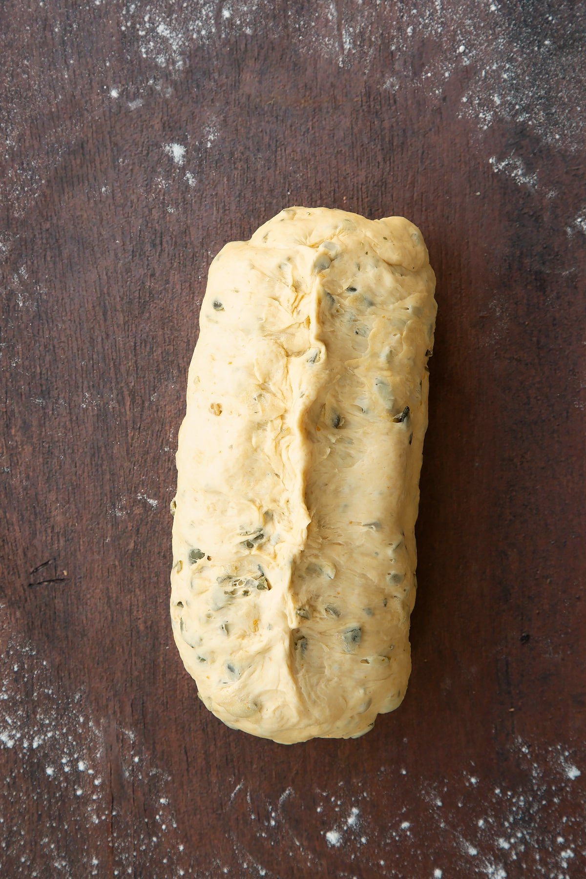 A roll of pumpkin seed bread dough, seam side up. The seam has been pinched to seal.