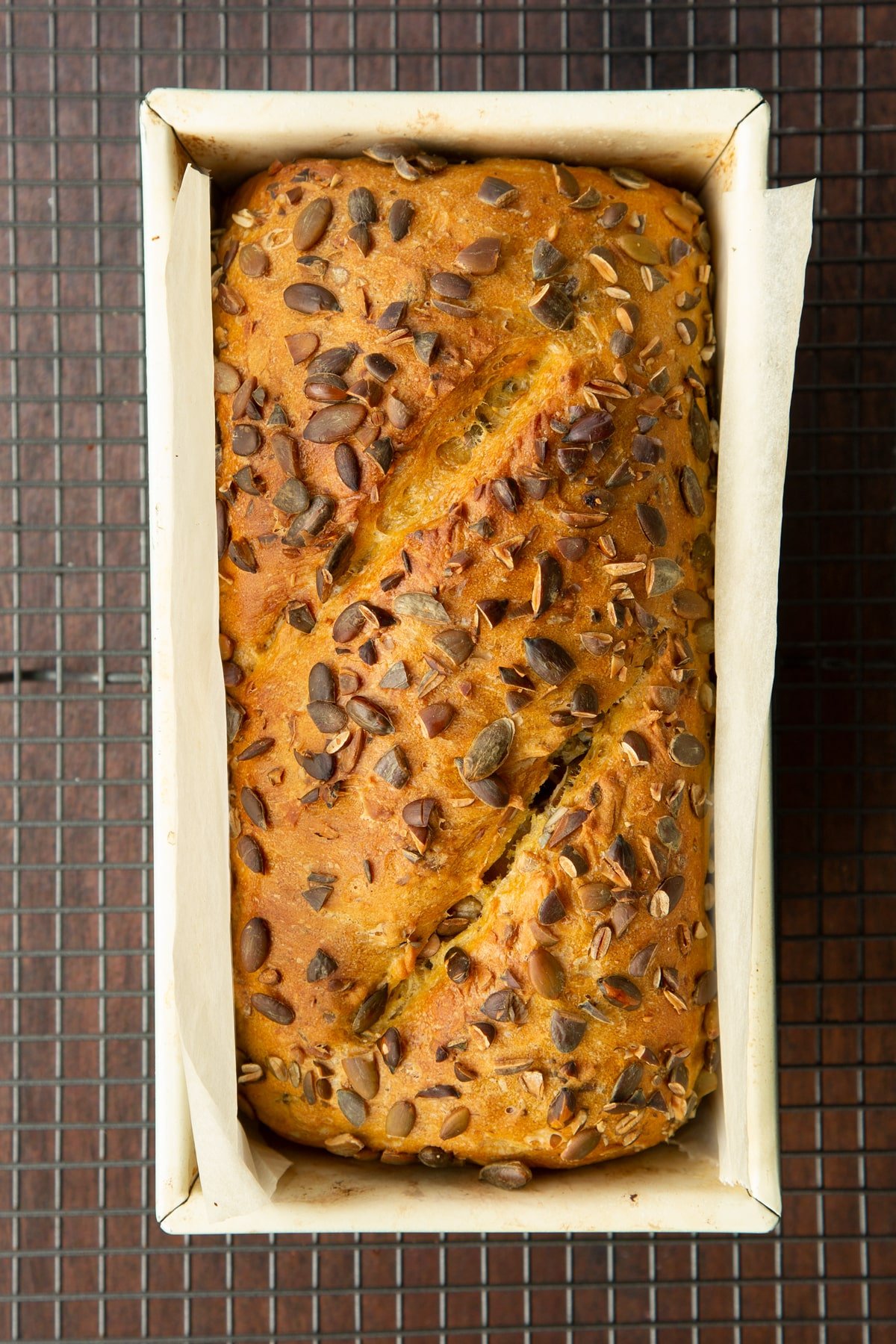 Freshly baked pumpkin seed bread in a loaf tin lined with baking paper.