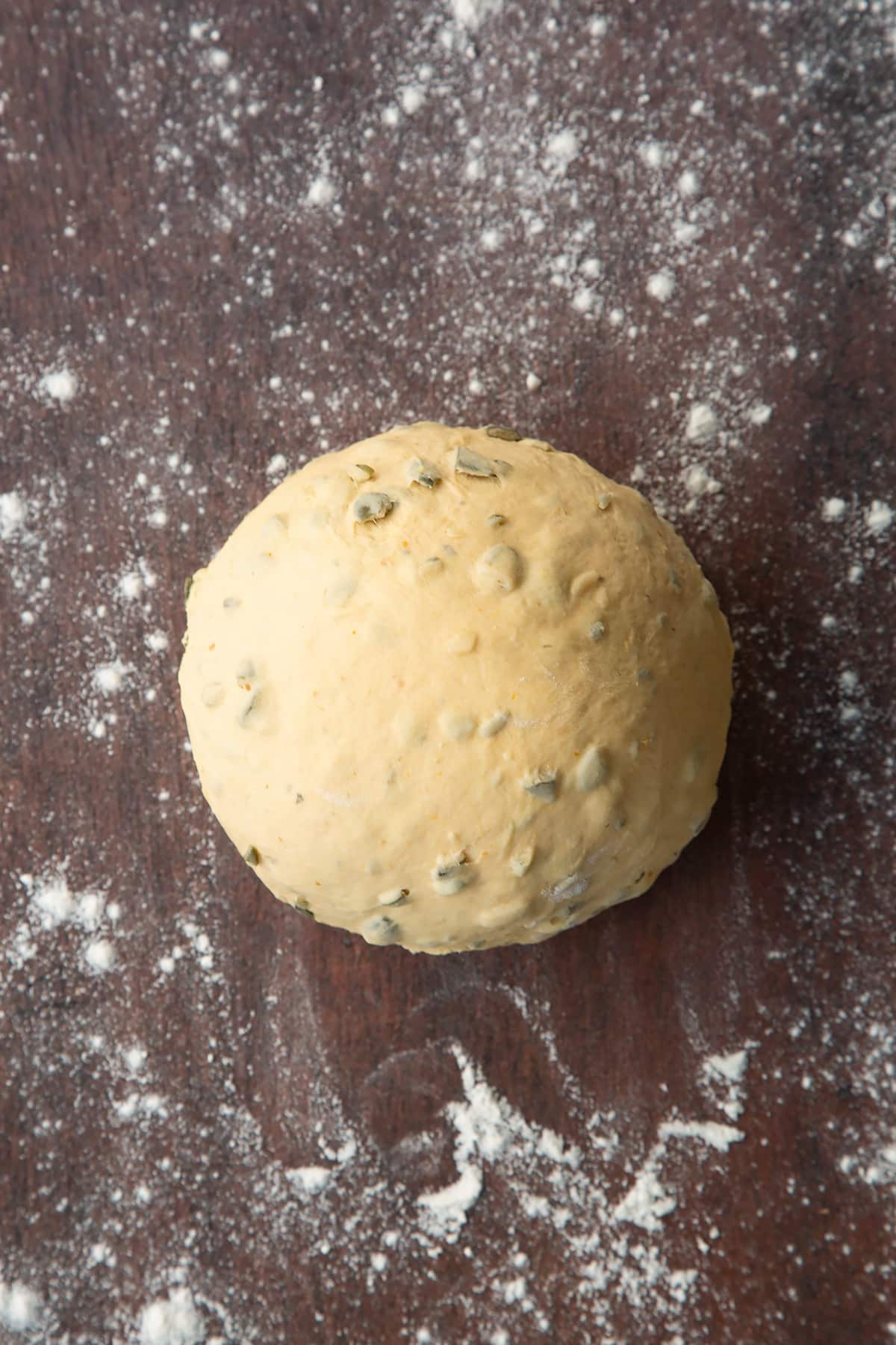 A ball of pumpkin seed bread dough on a floured surface.