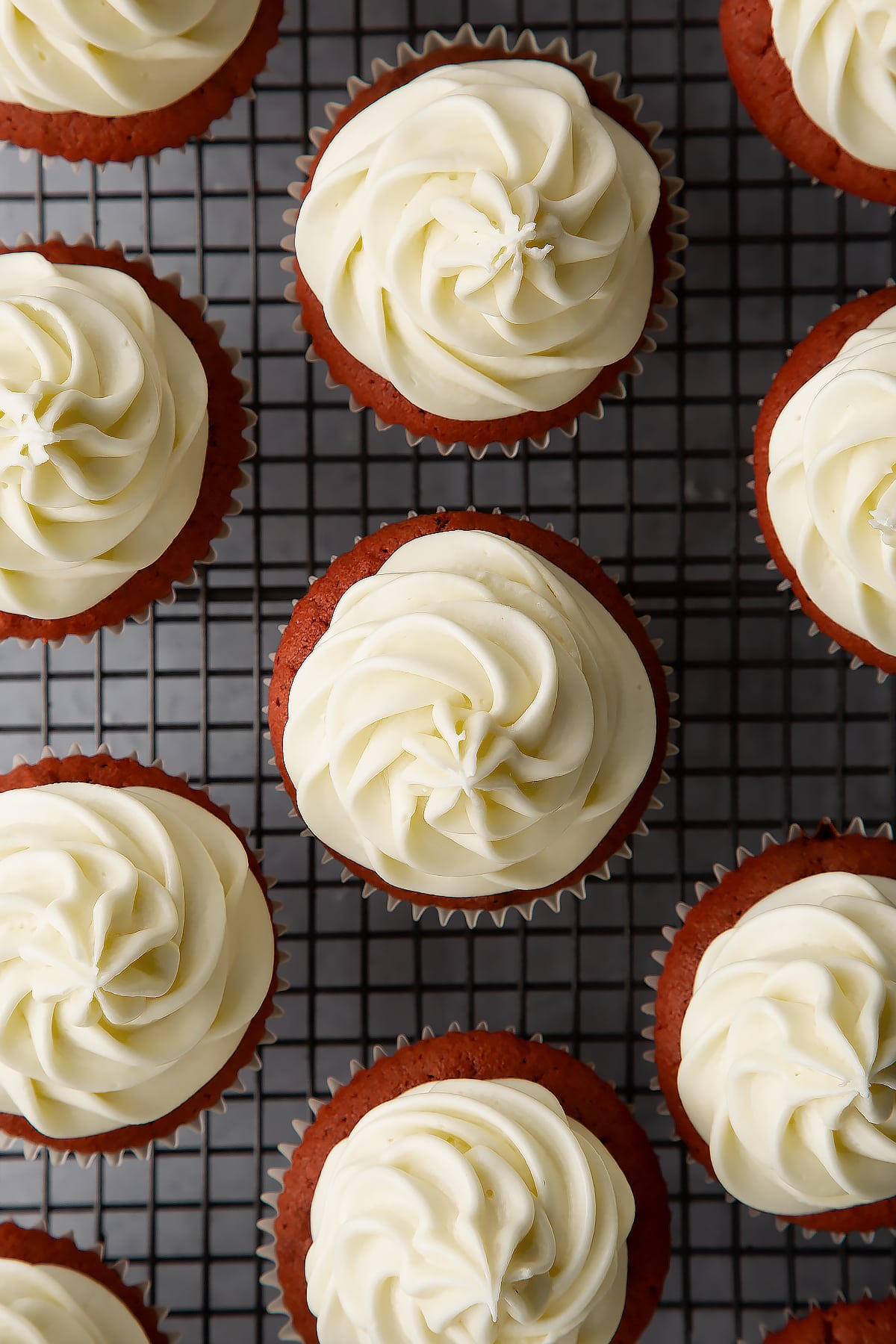 Cream cheese frosting piped on top of red velvet Halloween cupcakes on a wire rack.